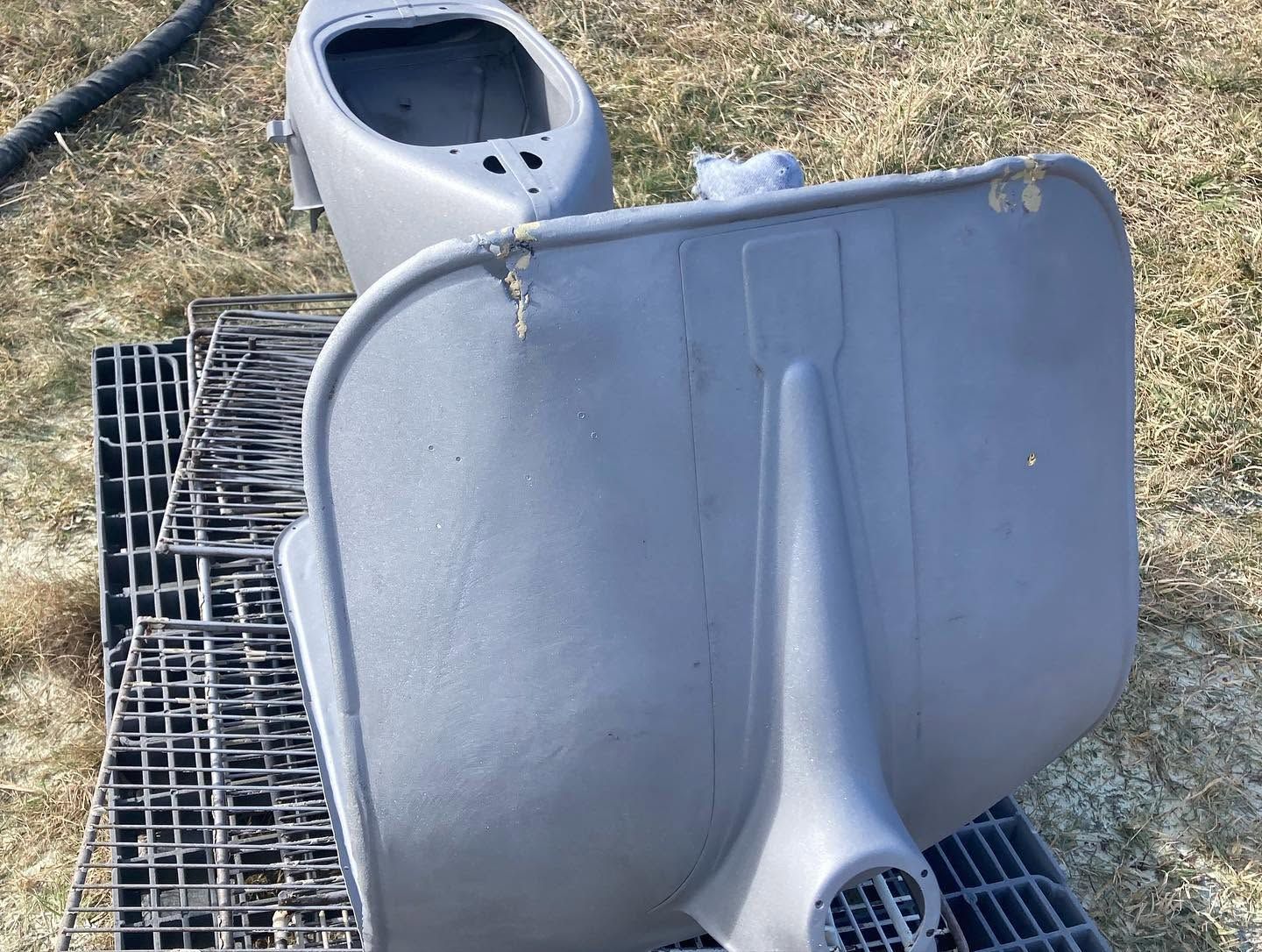 Gray plastic chair seat and backrest lying on grass beside a black metal grate.