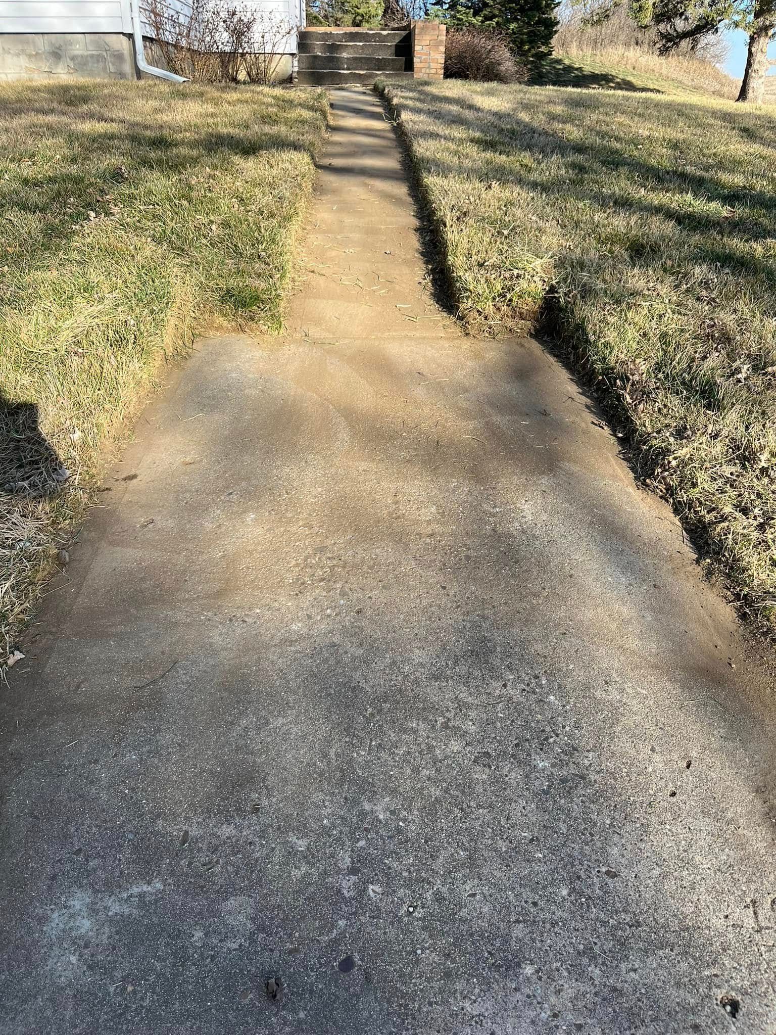 A concrete walkway leading to a house with stairs.