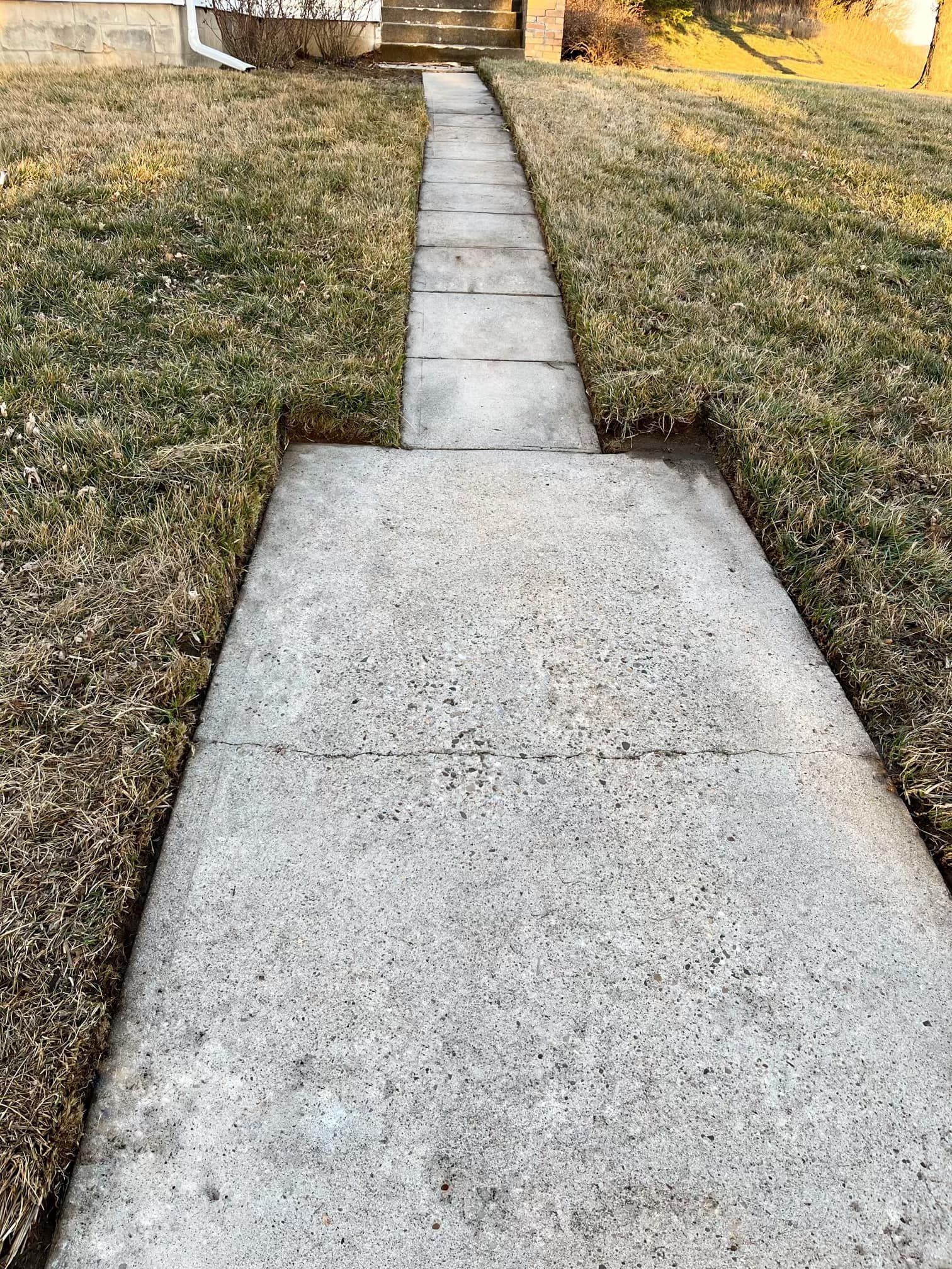 A concrete walkway leading to a house surrounded by grass.