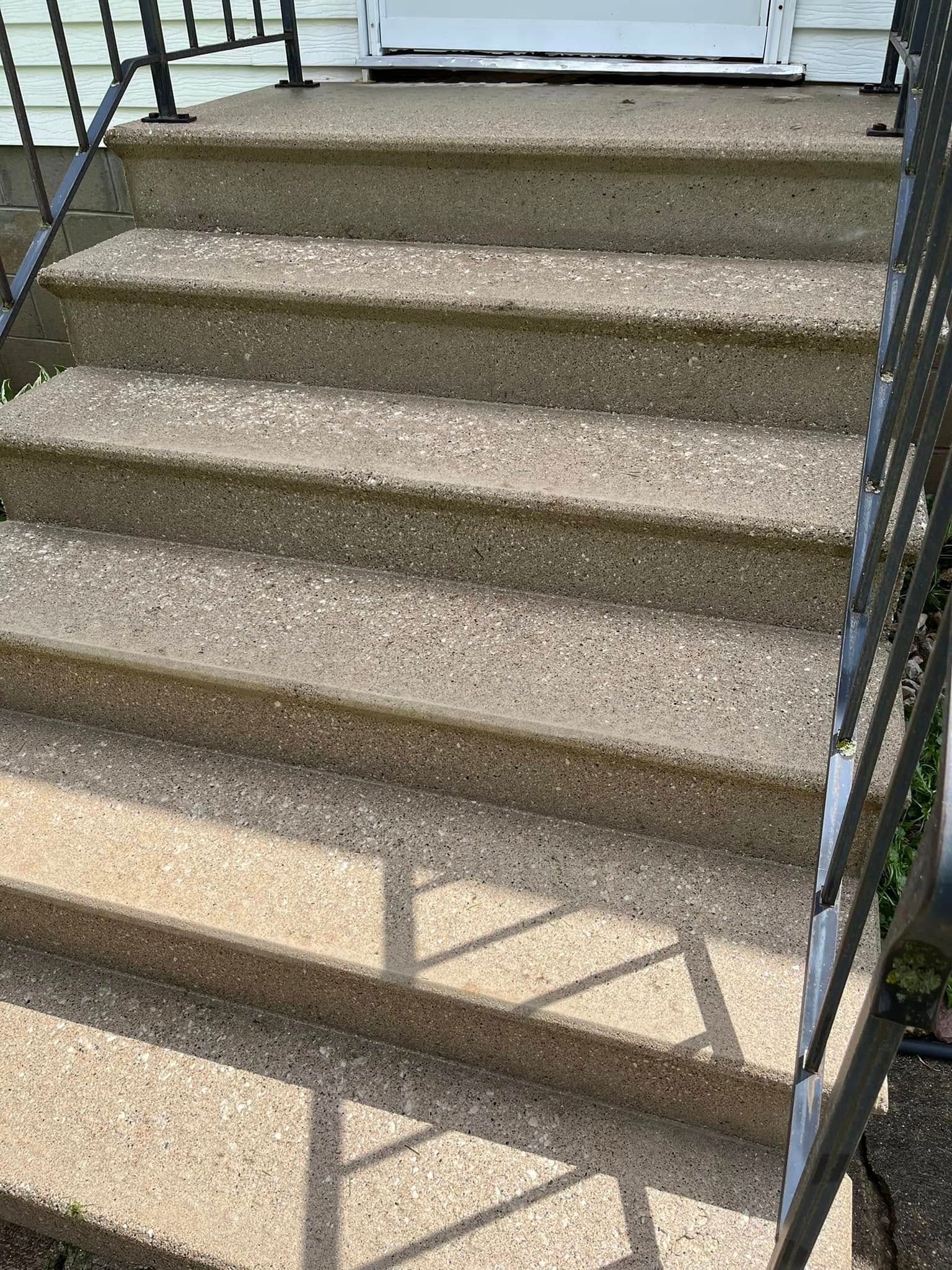 A set of concrete stairs leading up to a house with a metal railing.