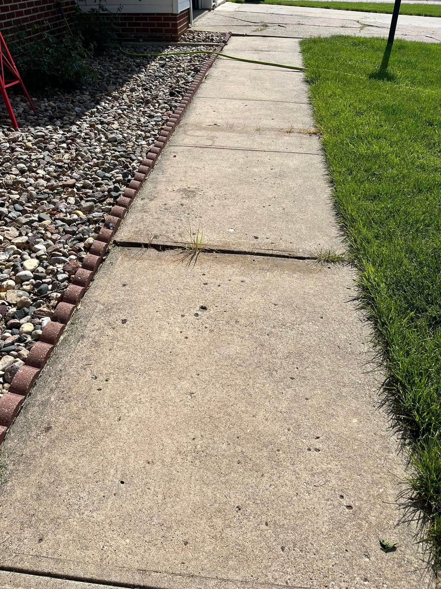 A sidewalk leading to a house with grass and rocks on the side.