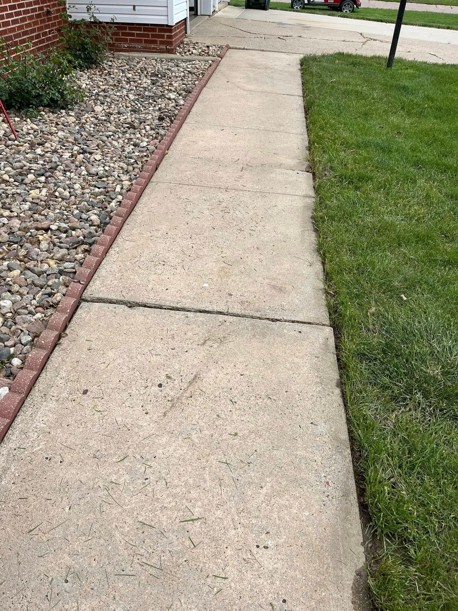 A sidewalk leading to a house with a lawn mower in the background.