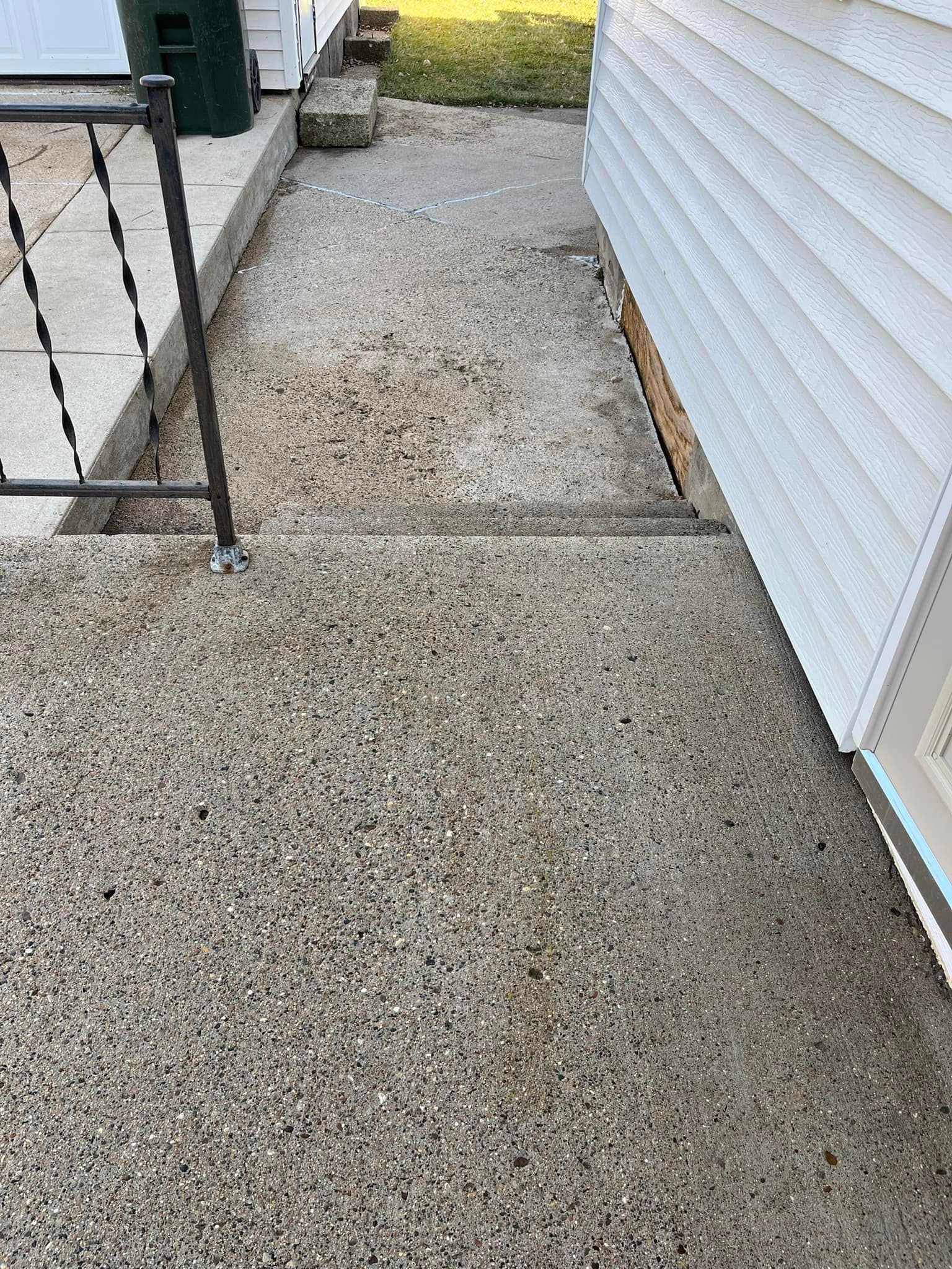 A concrete walkway next to a house with stairs leading up to it.