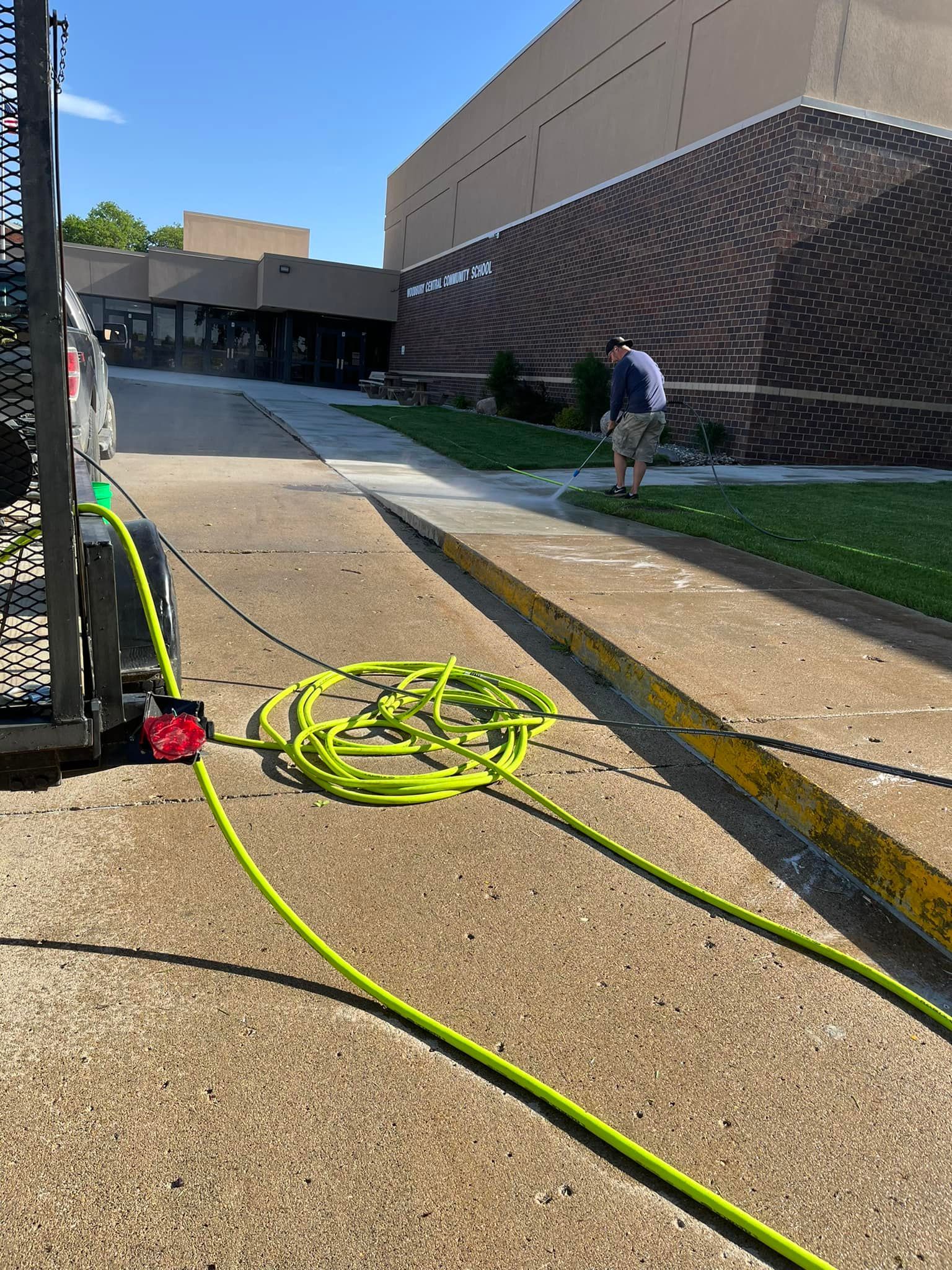 A man is standing on a sidewalk next to a truck with a hose attached to it.