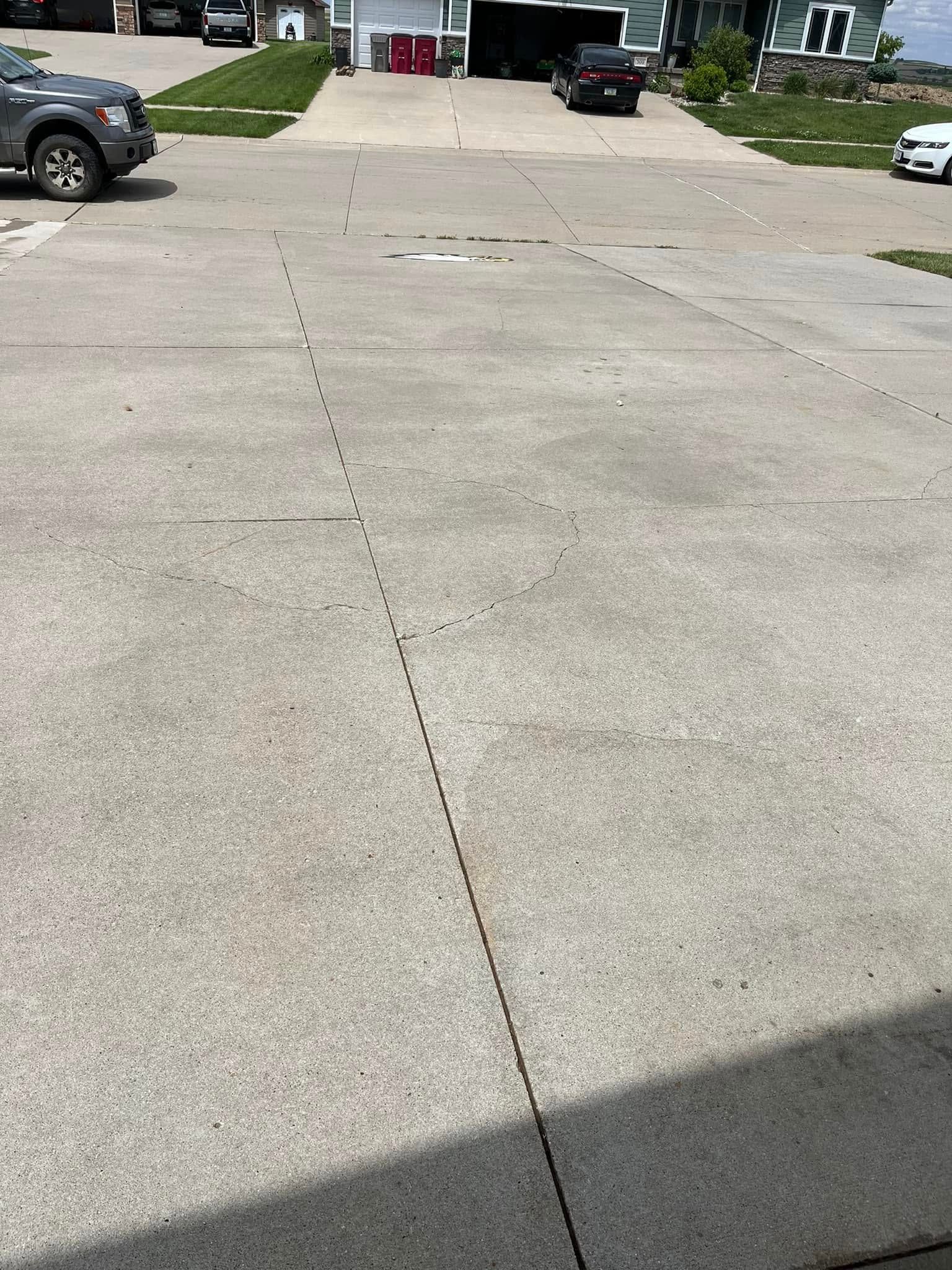 A concrete driveway with cars parked on it and a house in the background.