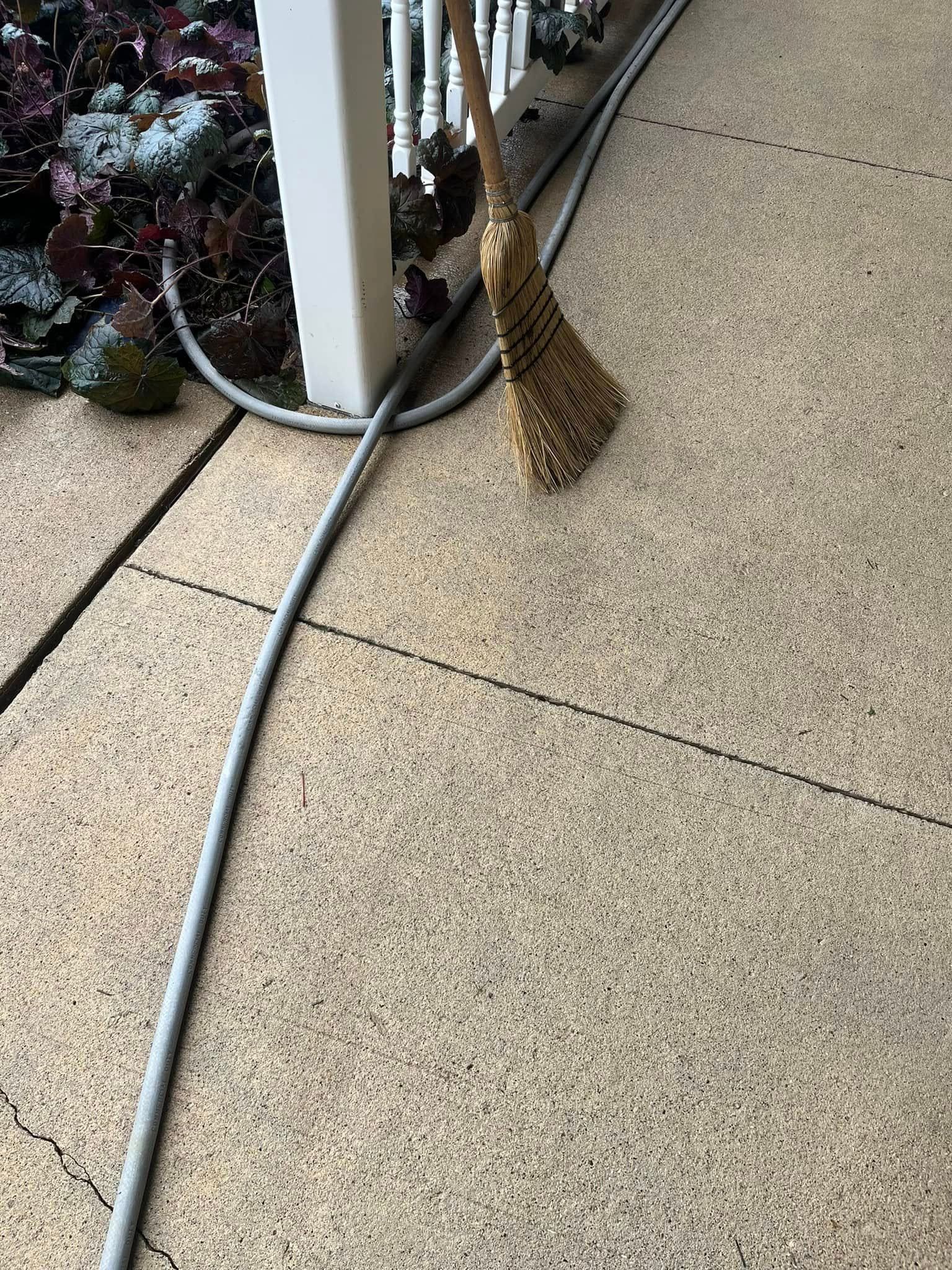 A broom is sitting next to a hose on a patio.