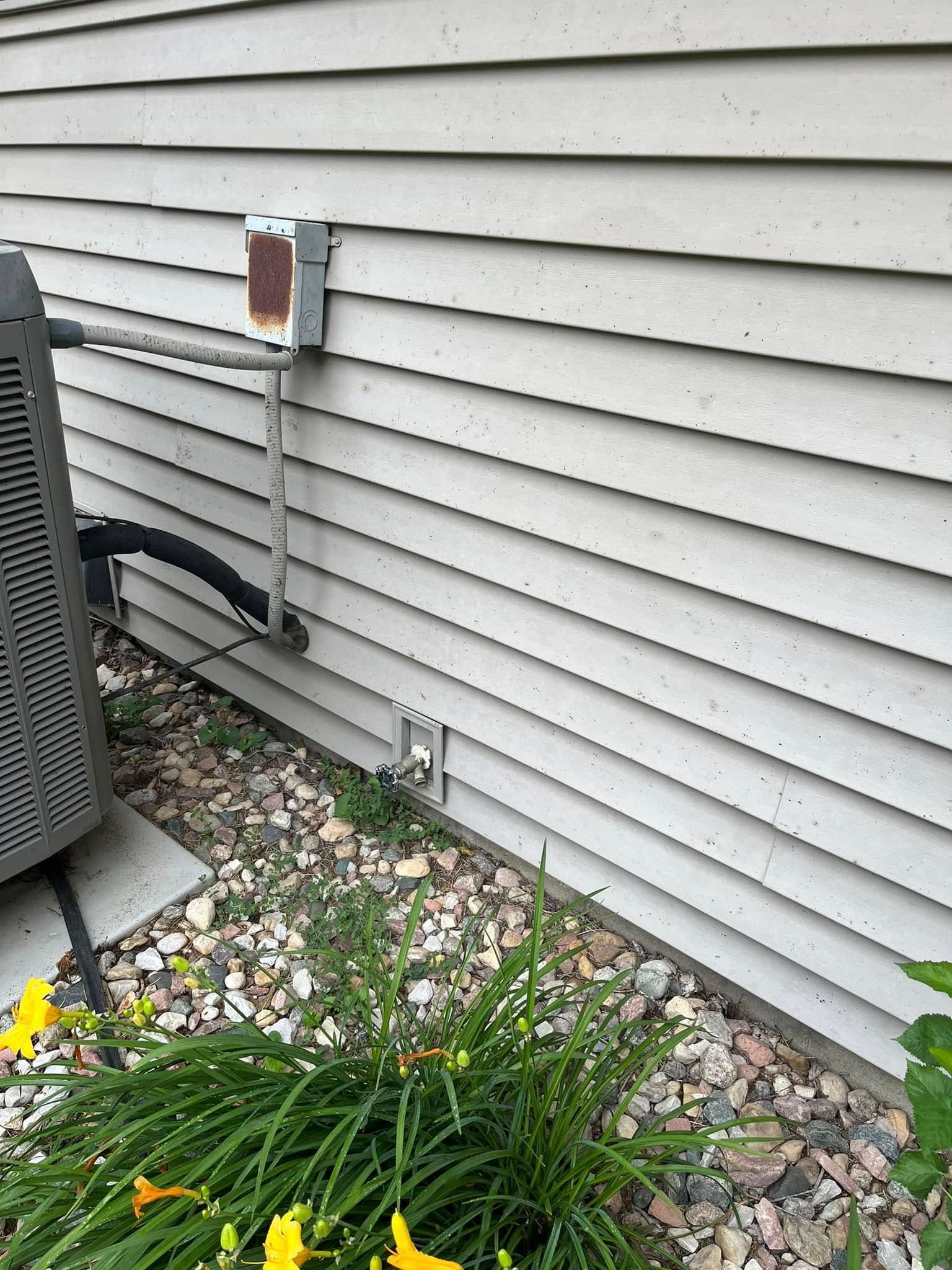 An air conditioner is sitting on the side of a house next to a flower bed.
