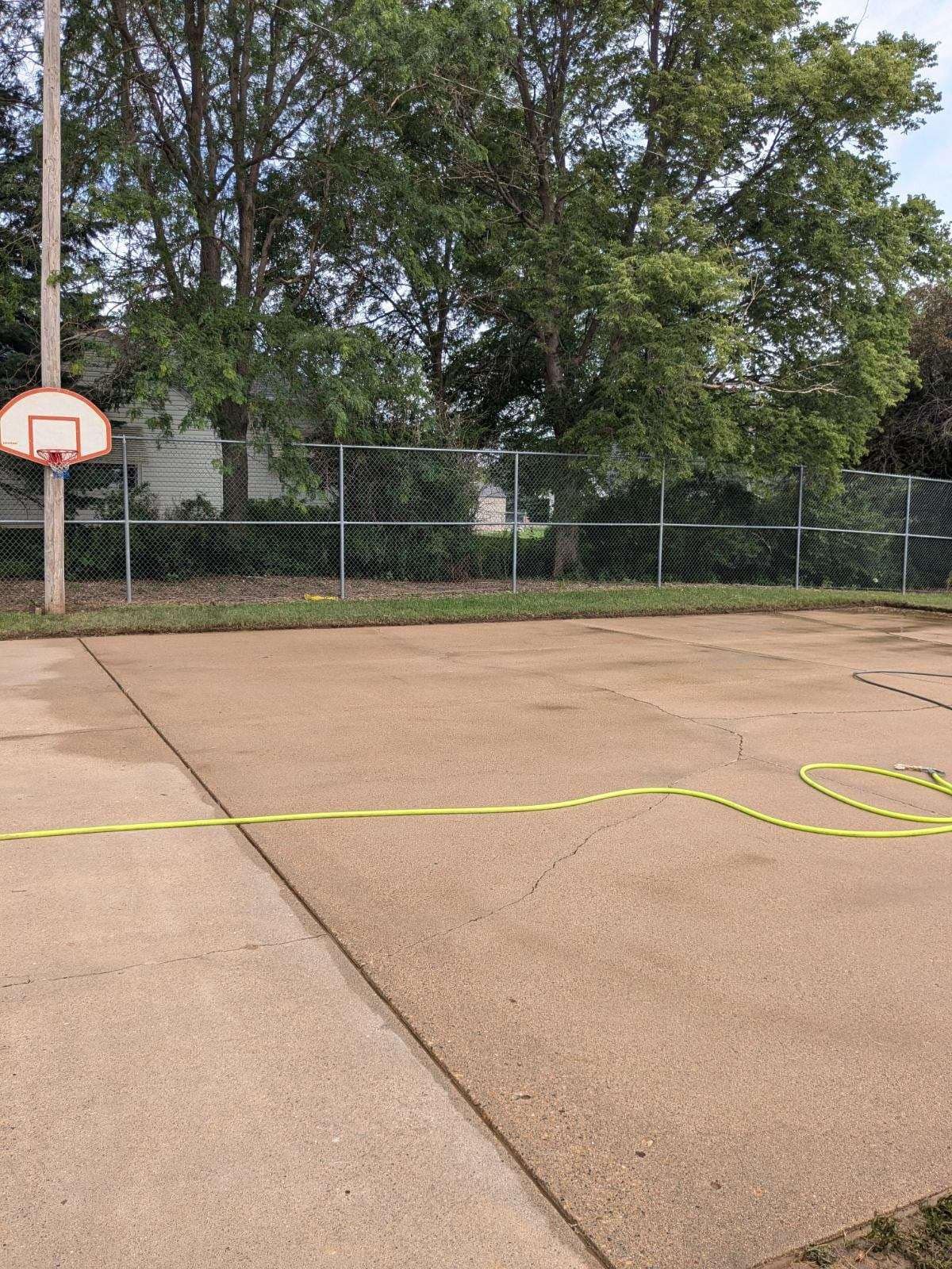 A basketball court with a fence and trees in the background.