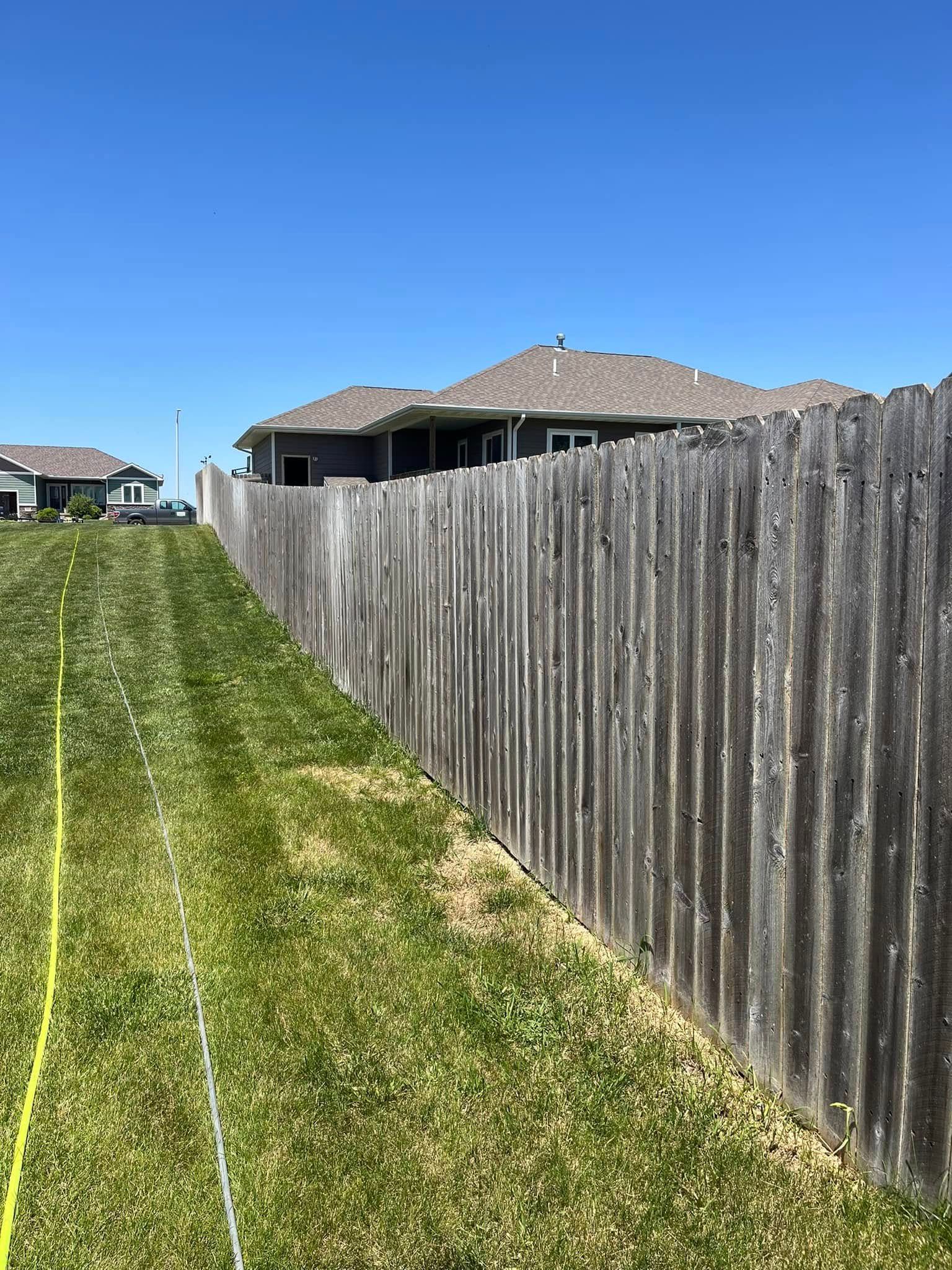 A wooden fence surrounds a lush green field with a house in the background.