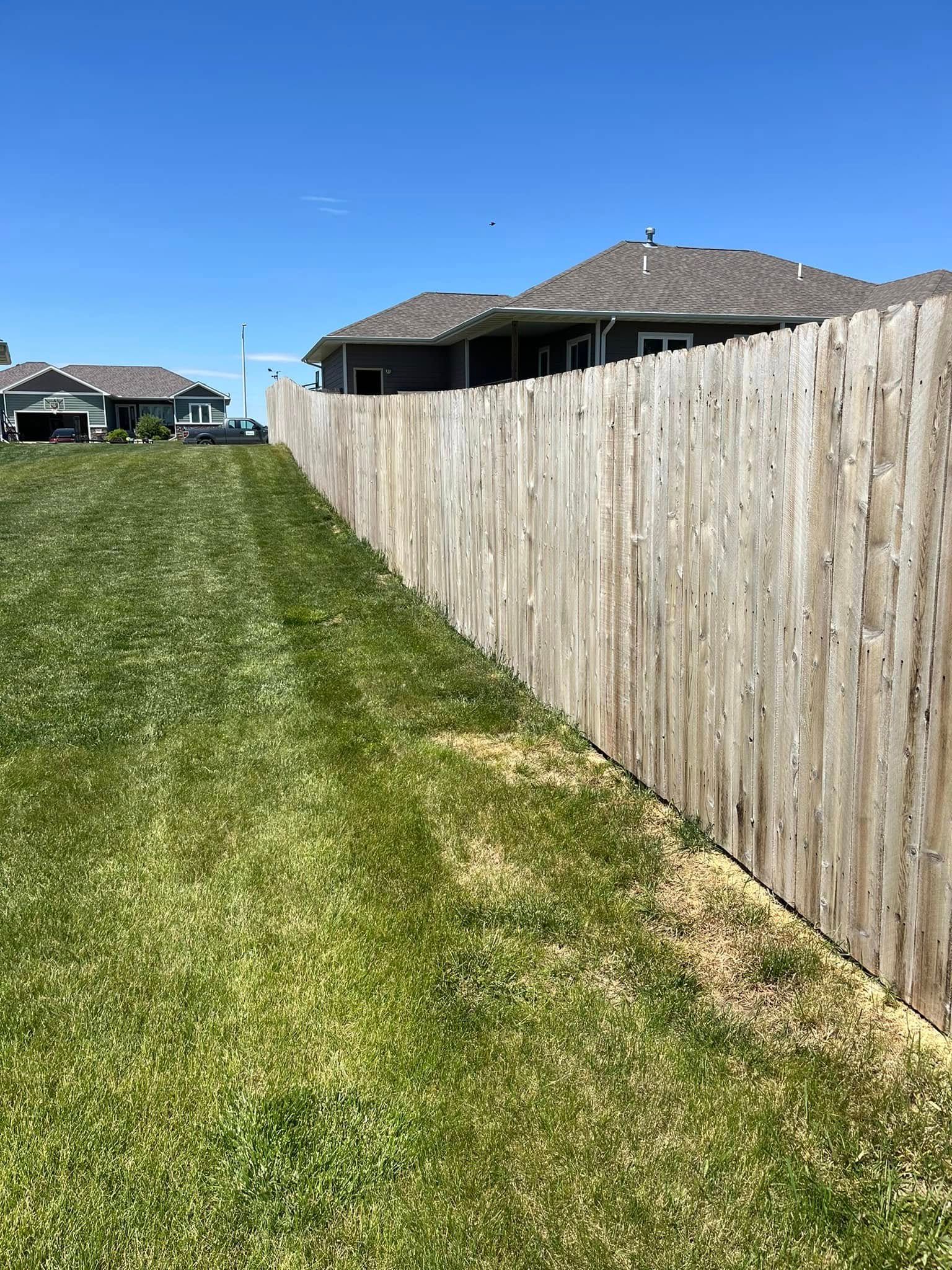 A wooden fence surrounds a lush green field with houses in the background.