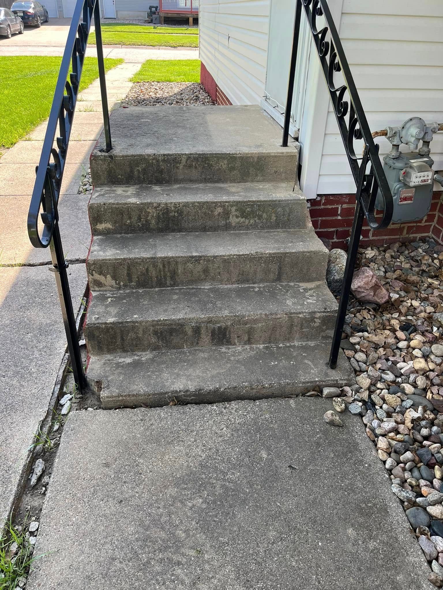 A set of concrete stairs leading up to a house with a metal railing.