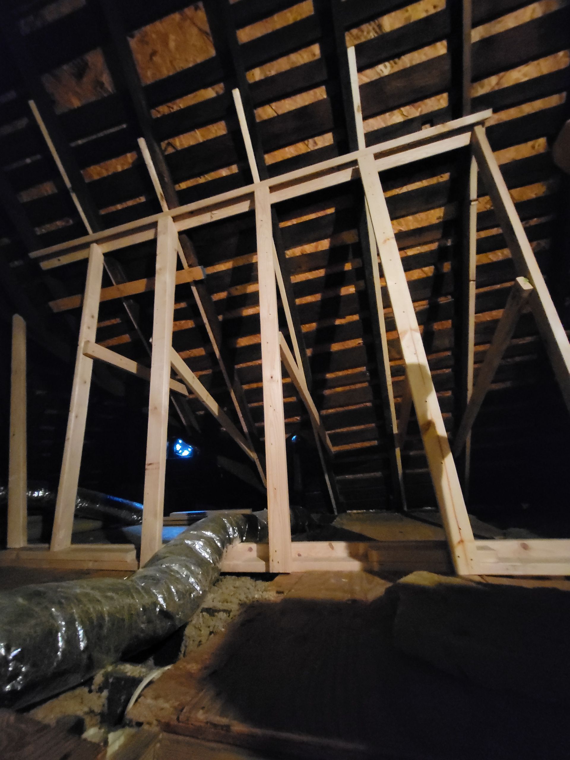 New wooden wall framing installed inside an attic space near flexible HVAC ductwork.
