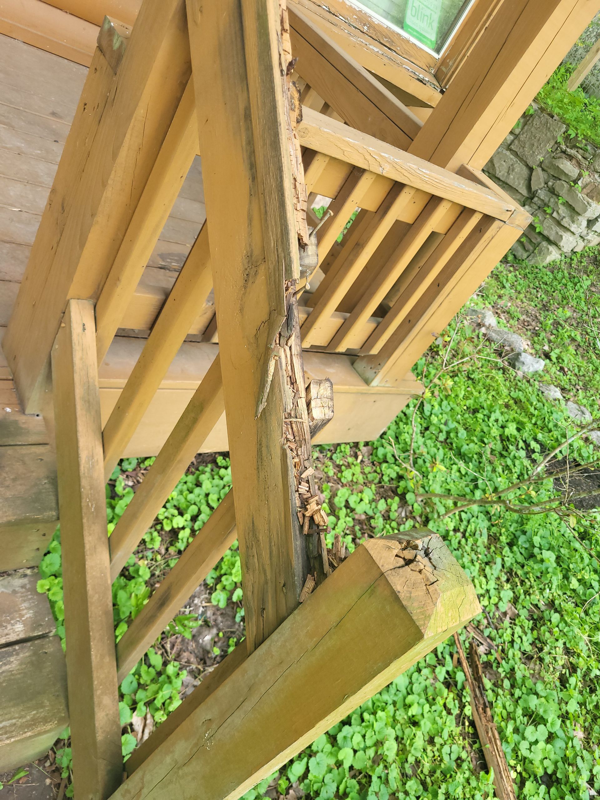 A section of a wooden deck railing is severely damaged and splintered, with rot and insect infestation visible.