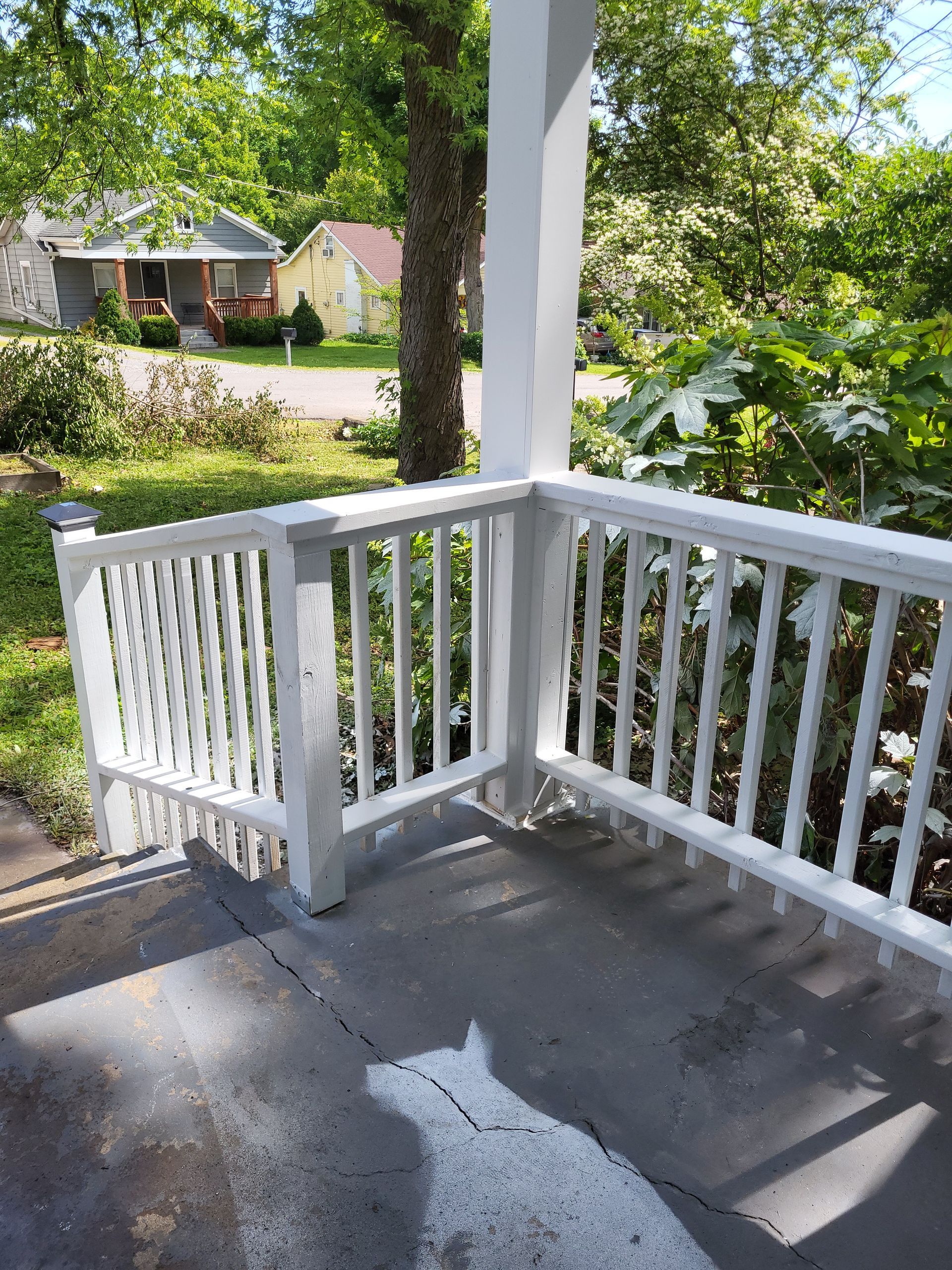 A view from a white-railed wooden porch looking down at a concrete floor with a cat-shaped shadow and a neighborhood view.