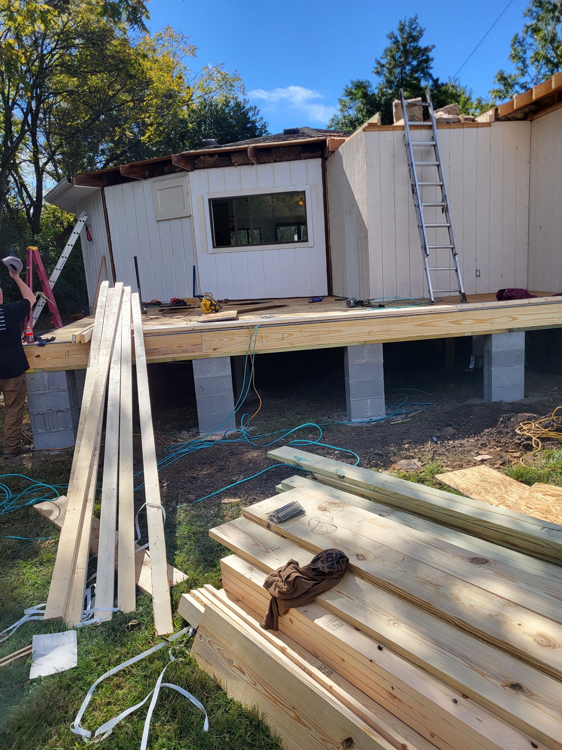 Construction workers frame a wooden deck attached to the side of a building supported by concrete blocks.
