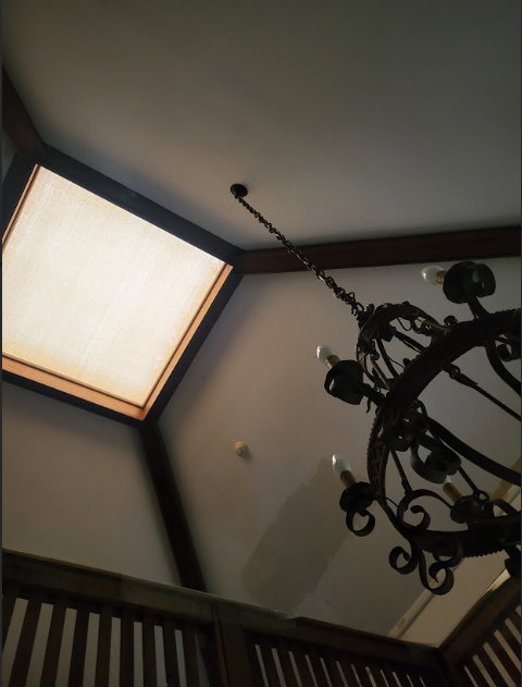 Low-angle view of a wrought iron chandelier hanging from a vaulted ceiling with a square skylight and wooden beams.