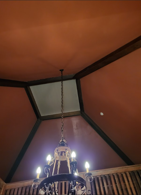 A chandelier hangs beneath a square skylight set in a vaulted, terracotta-colored ceiling with dark wooden beams.
