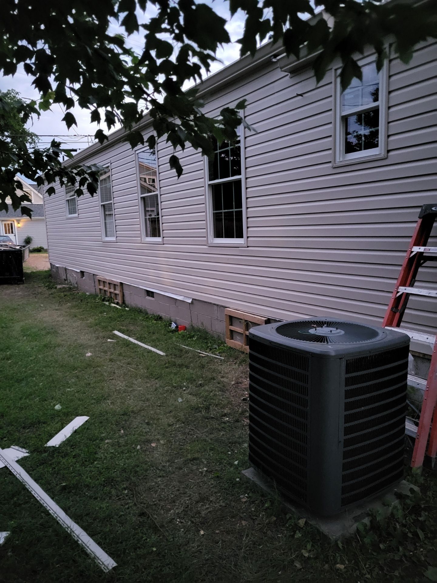 Exterior wall of a light-colored, vinyl-sided home with several windows, a central AC unit, and a ladder on the right.