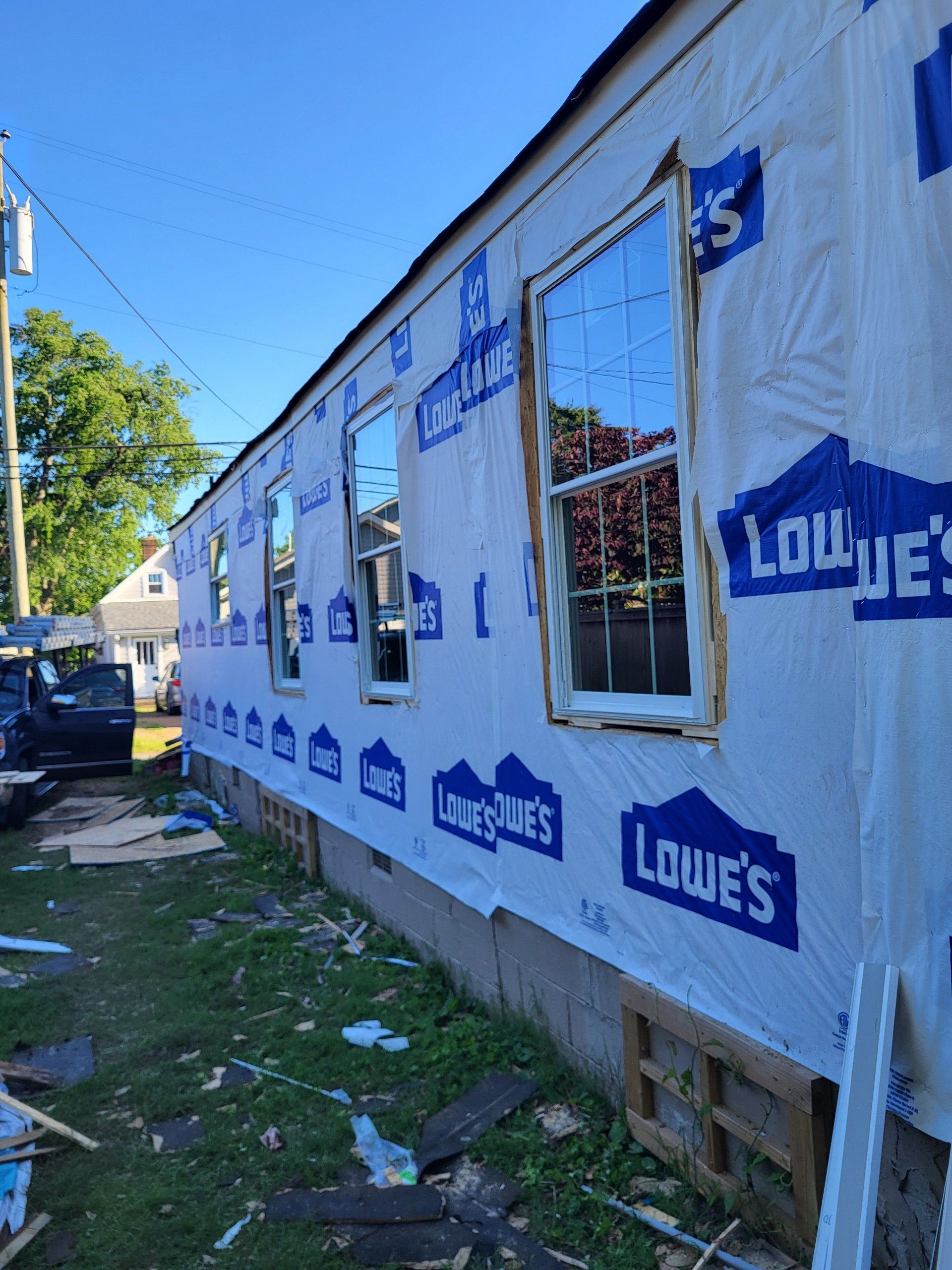 Exterior wall of a house under renovation, covered in Lowe’s branded house wrap with three windows installed.