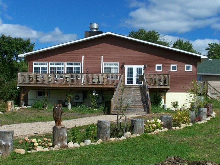 Red house with wooden deck and stone steps on a grassy hillside under a blue sky