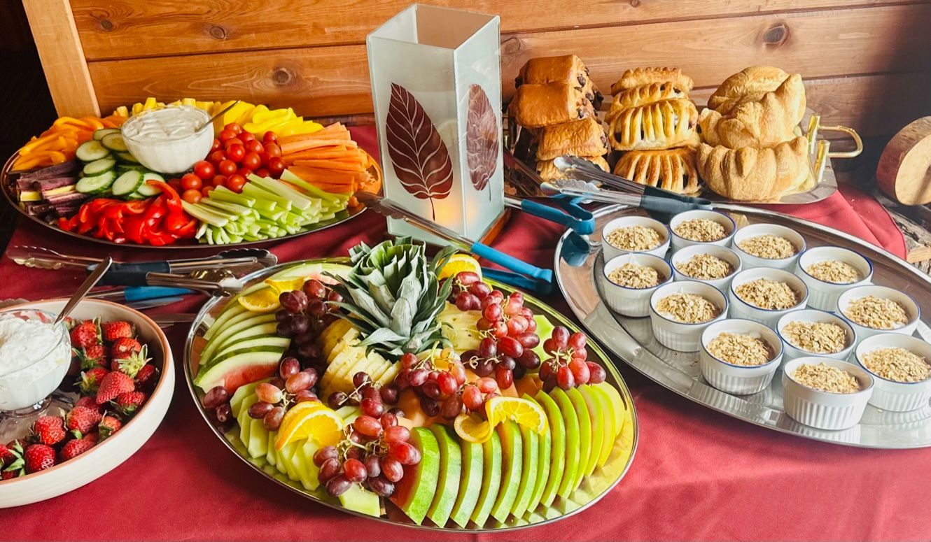 Buffet table with fruit platters, pastries, and dessert cups on a red tablecloth against wood walls