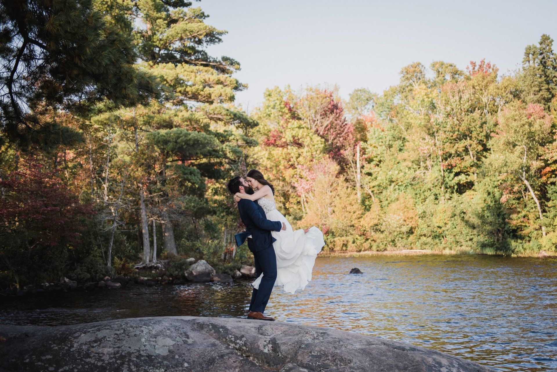 Couple embracing by a lakeshore with autumn trees in the background
