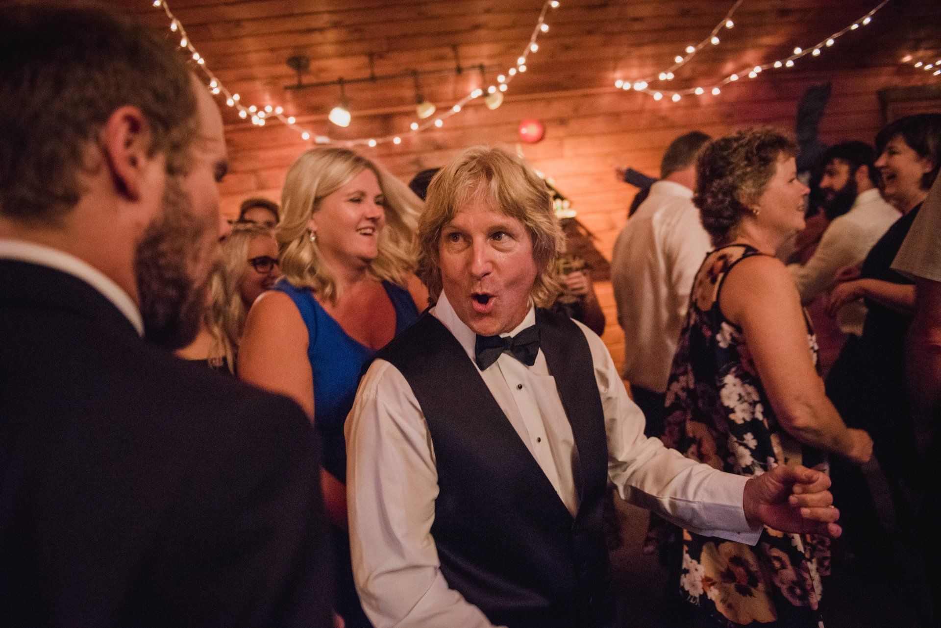 People dancing at a lively indoor party with string lights and warm wood-paneled walls