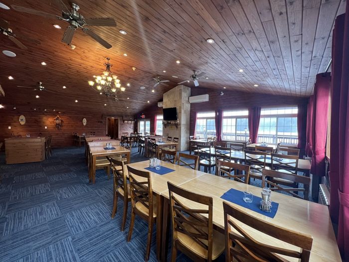 Rustic restaurant dining room with wooden tables, chairs, blue carpet, chandeliers, and large windows