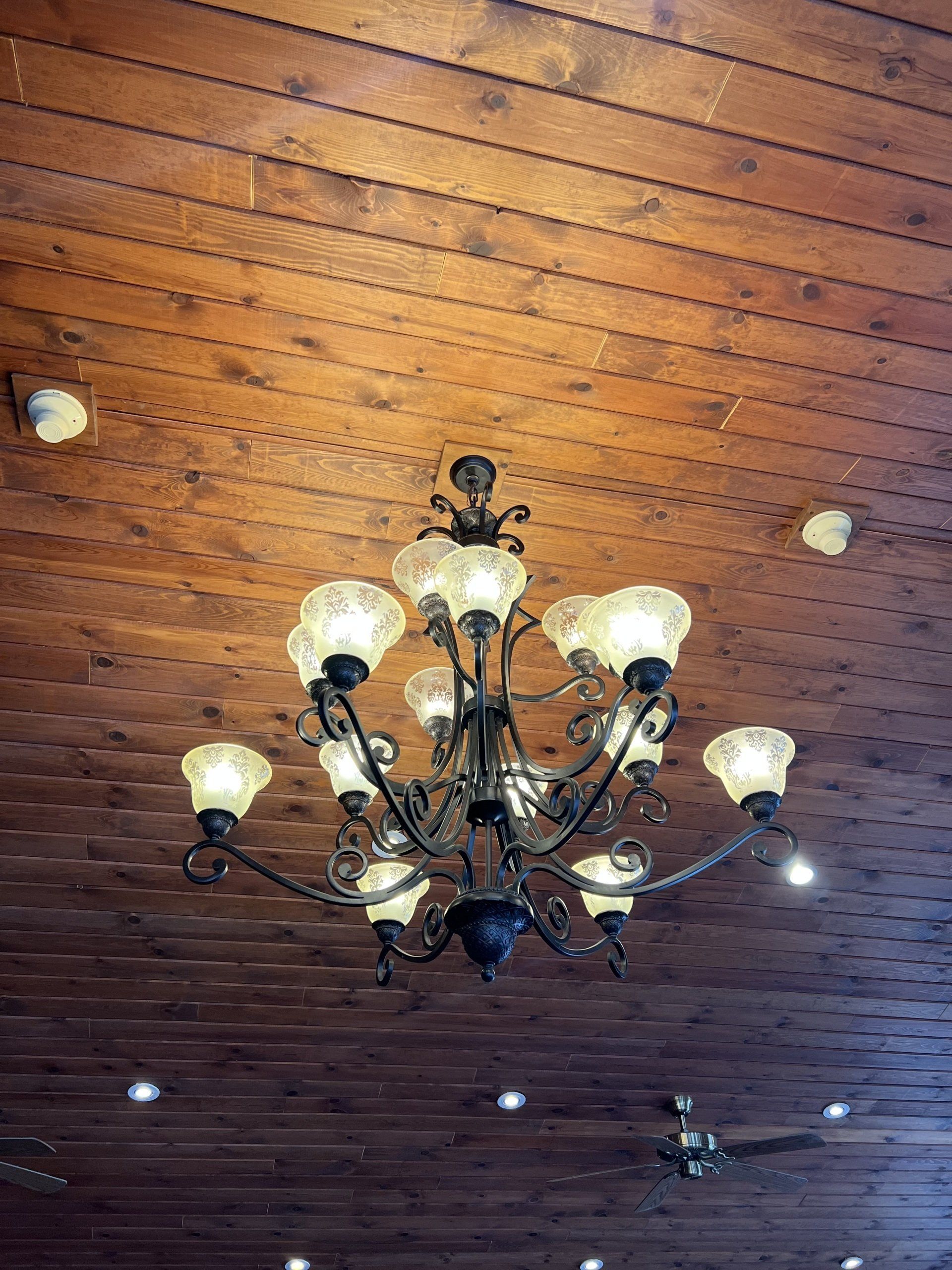 Ornate chandelier with lit bulbs hanging from a wooden plank ceiling