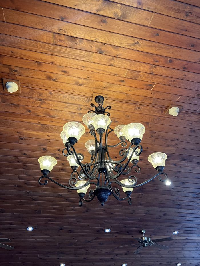 Ornate chandelier with glowing bulbs hanging from a wooden ceiling