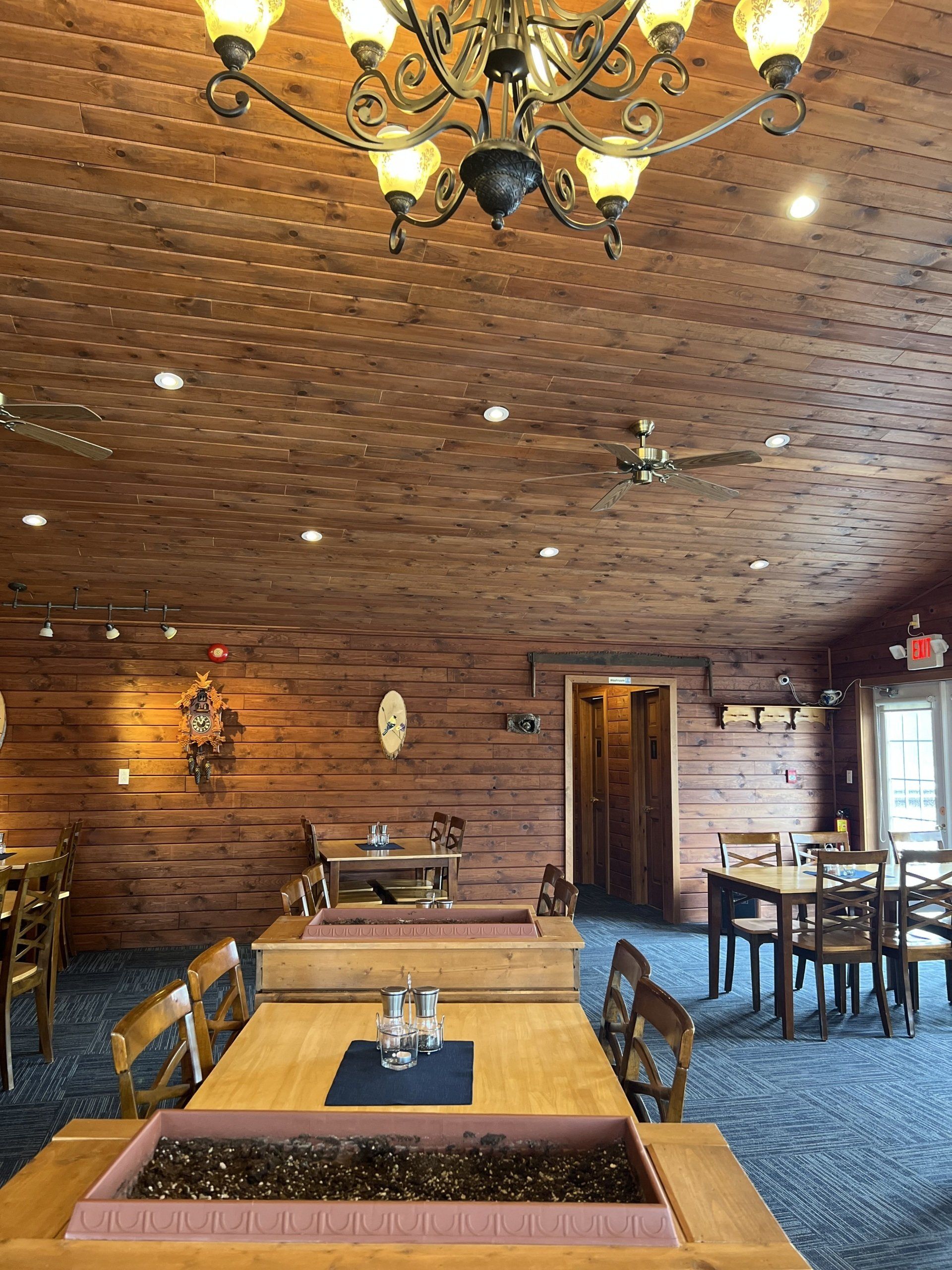 Wood-paneled restaurant dining room with rustic tables, chairs, and a chandelier-lit ceiling