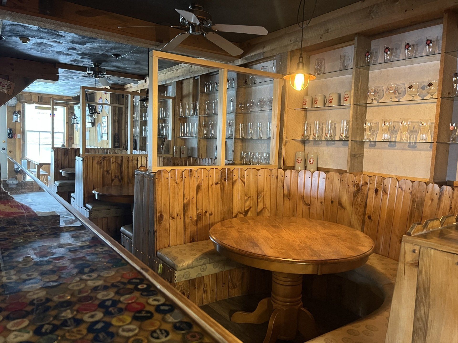 Empty rustic bar interior with wood paneling, glass cases, and a round wooden table.