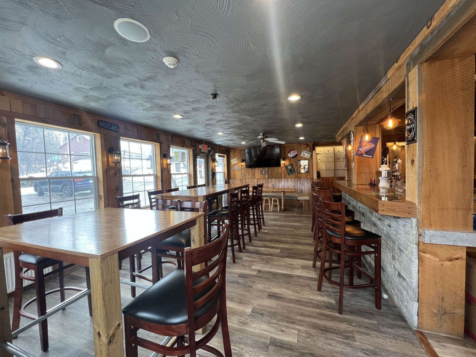 Empty restaurant dining room with wooden tables, stools, and a stone bar counter under warm lighting.