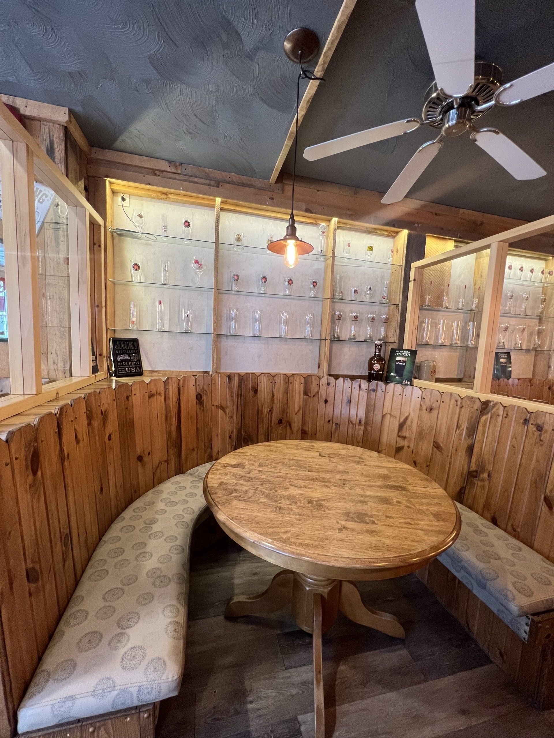 Cozy wooden booth with round table, padded bench seating, and ceiling fans in a rustic restaurant.