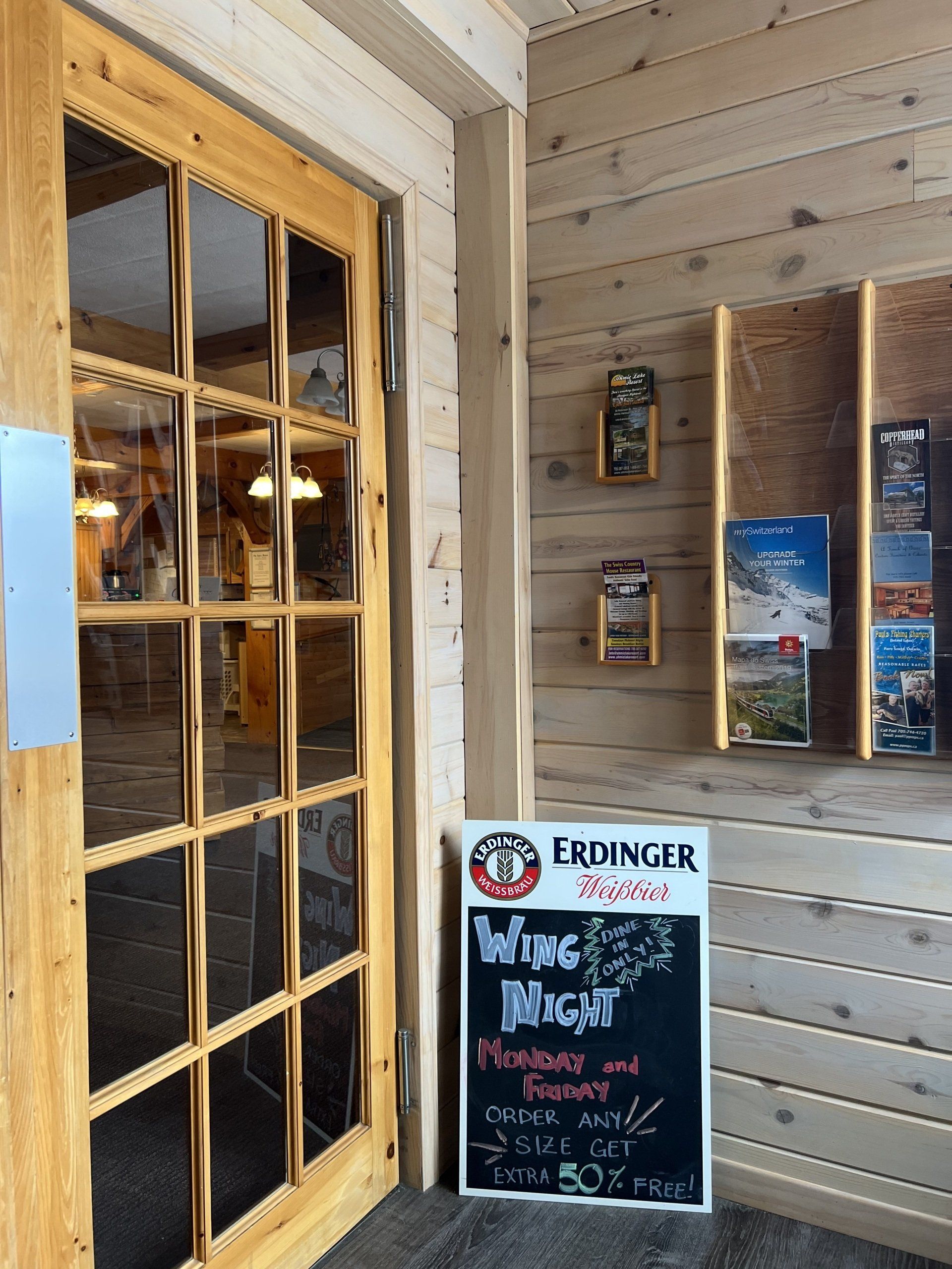 Wooden storefront entrance with glass door and a chalkboard sign outside on a porch.