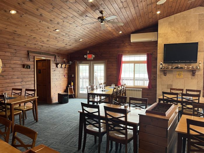 Empty rustic restaurant dining room with wooden tables, chairs, brick walls, and a TV above the fireplace