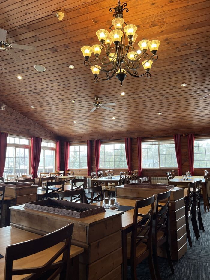 Elegant restaurant interior with chandeliers, patterned ceiling, wooden tables, and red curtains by large windows