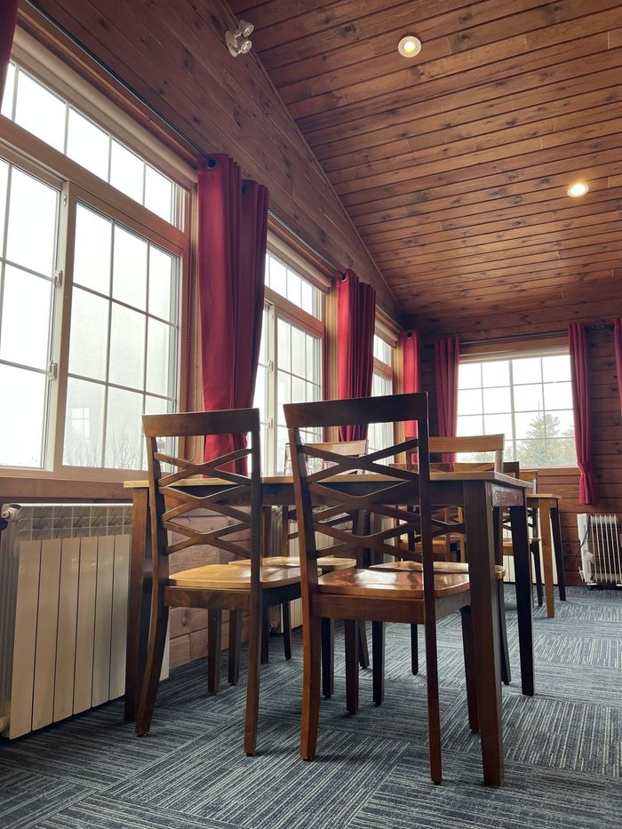Empty dining room with wooden chairs, red curtains, and large windows in warm light