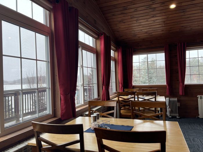 Cozy café dining room with large windows, burgundy curtains, wooden tables, and snowy outdoor view