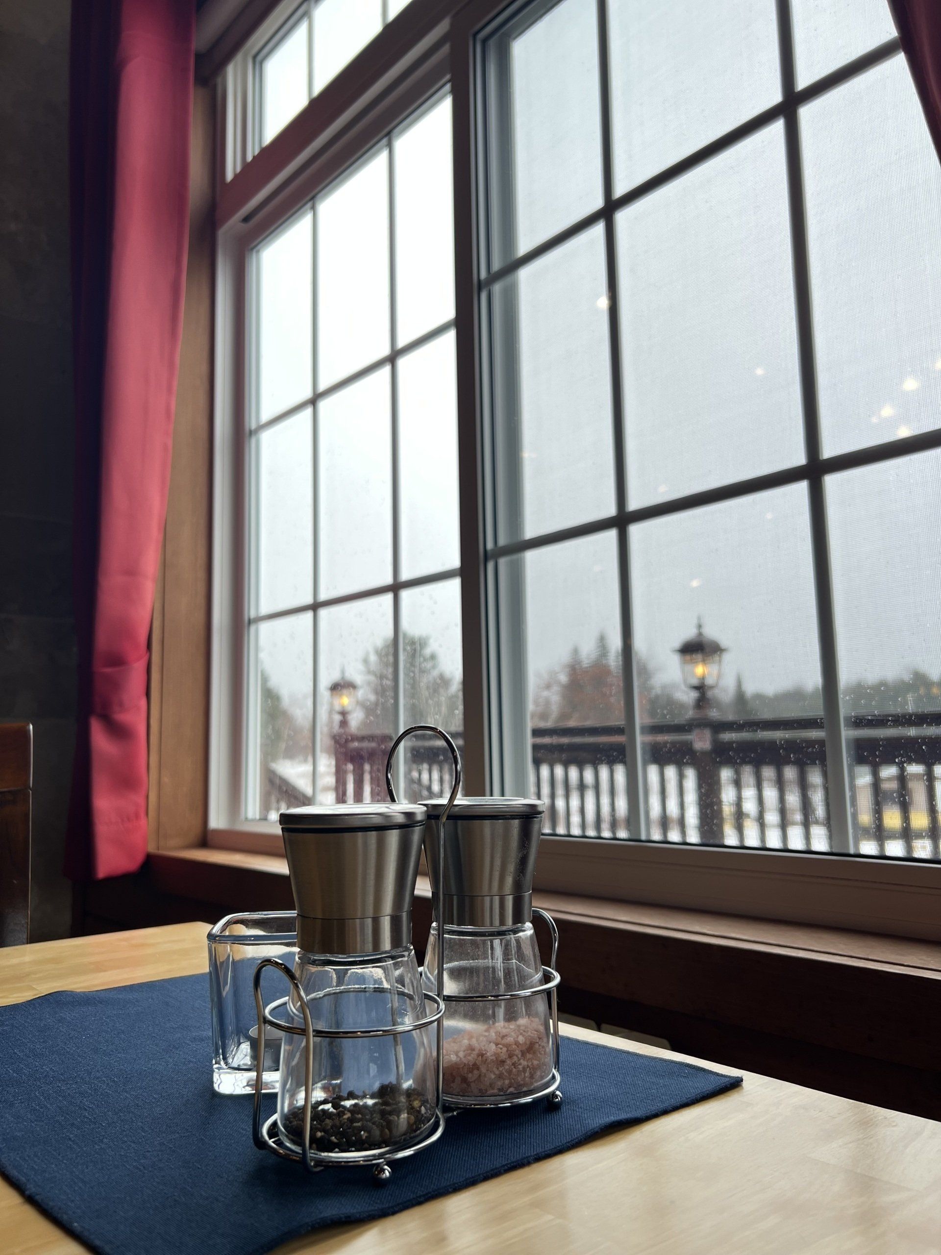 Two glasses on a blue placemat by a large window overlooking a snowy waterfront
