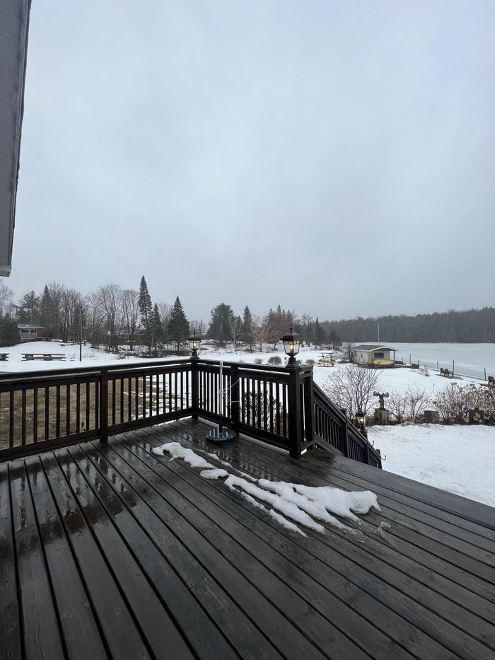 Snowy deck overlooking a frozen lake and trees under a gray sky