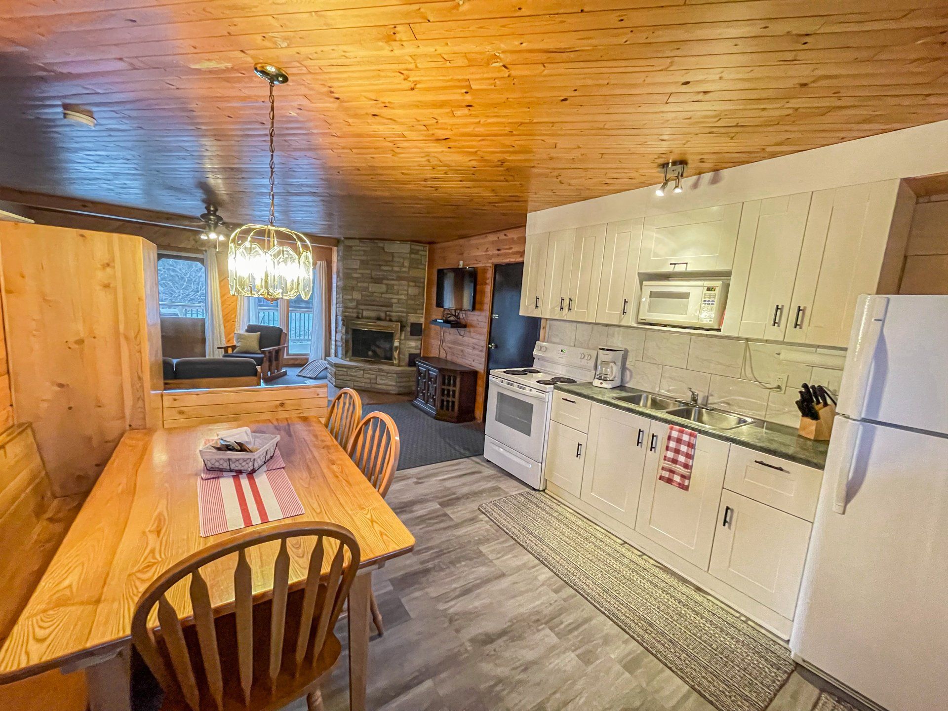 Rustic kitchen and dining area with wood-paneled walls, white appliances, and a wooden table under a chandelier