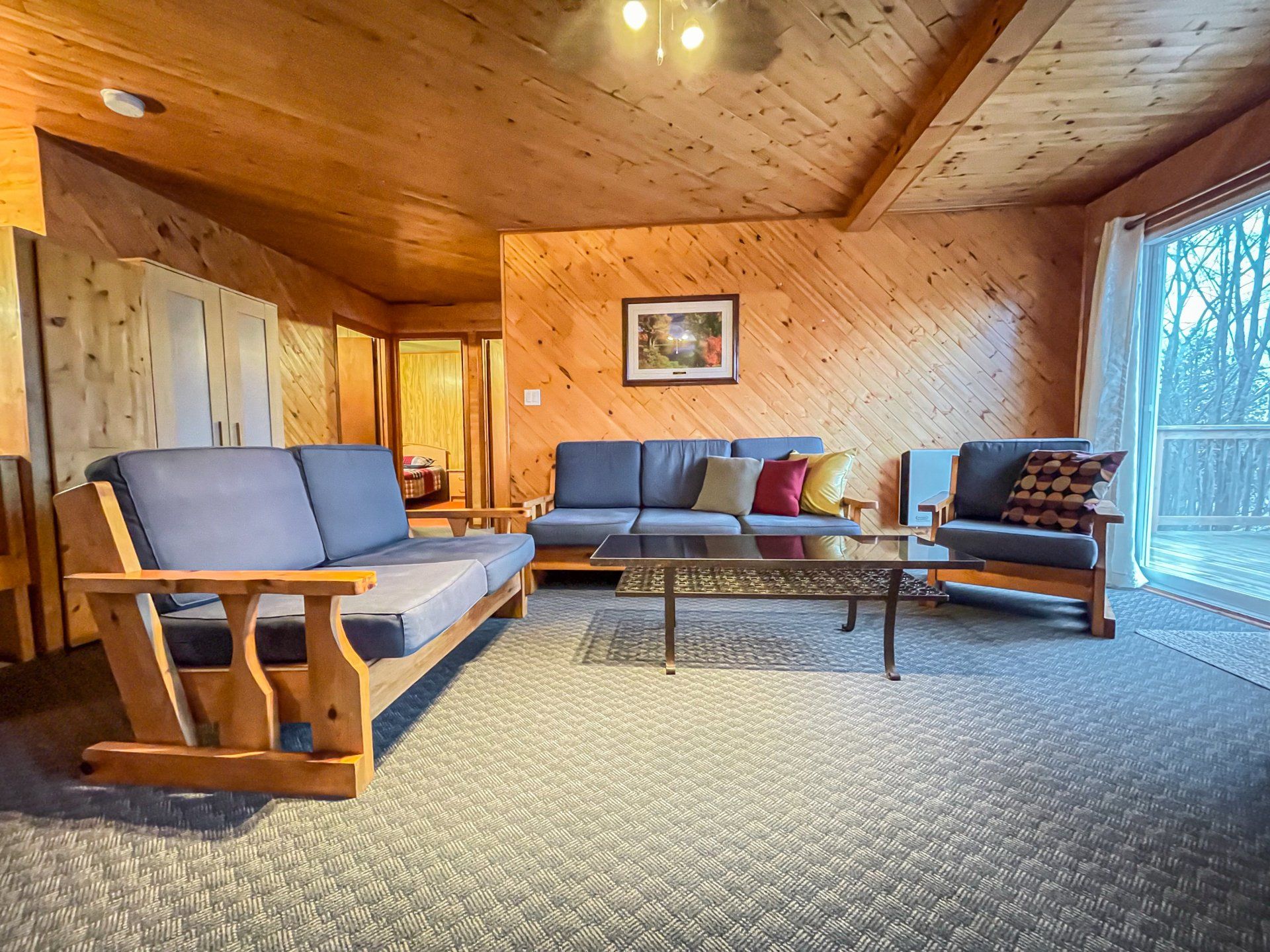 Cozy wood-paneled living room with blue-gray sofas, coffee table, lamp, and large windows