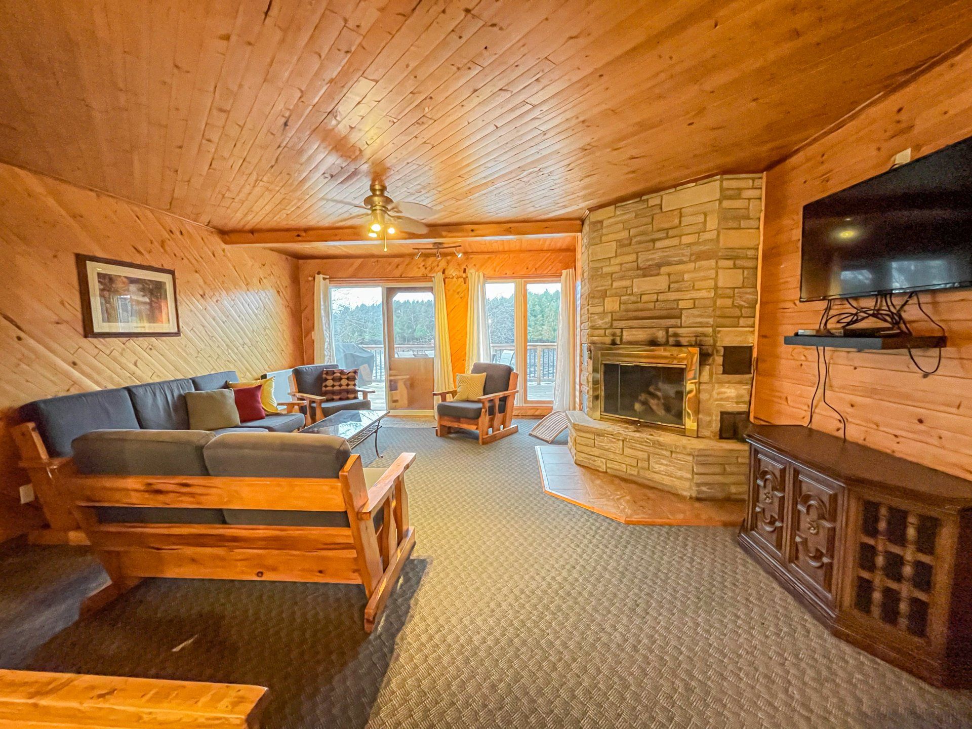 Cozy wood-paneled living room with stone fireplace, sectional sofa, and large windows