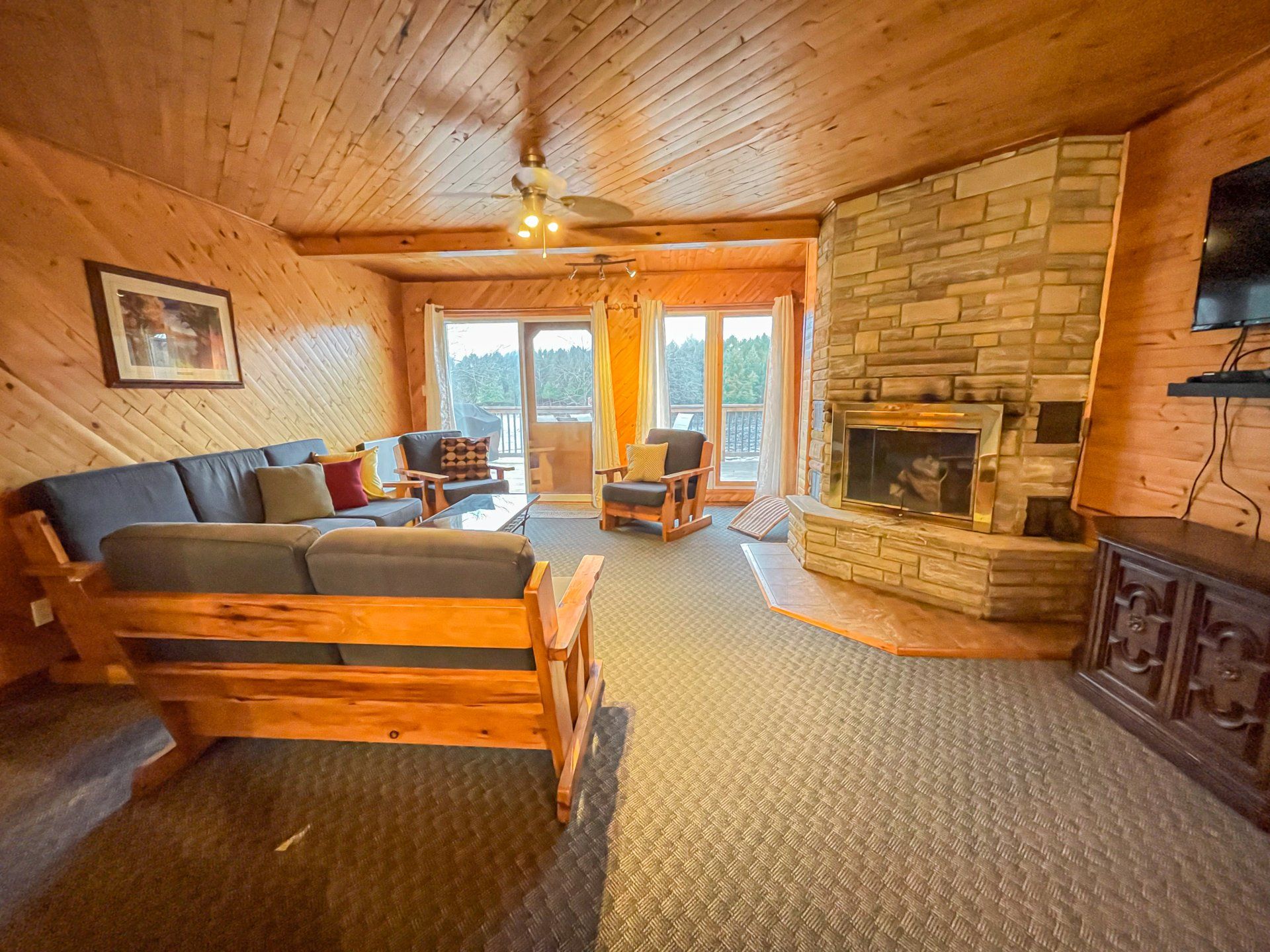 Cozy log cabin living room with stone fireplace, wood walls, blue sofa, and large windows