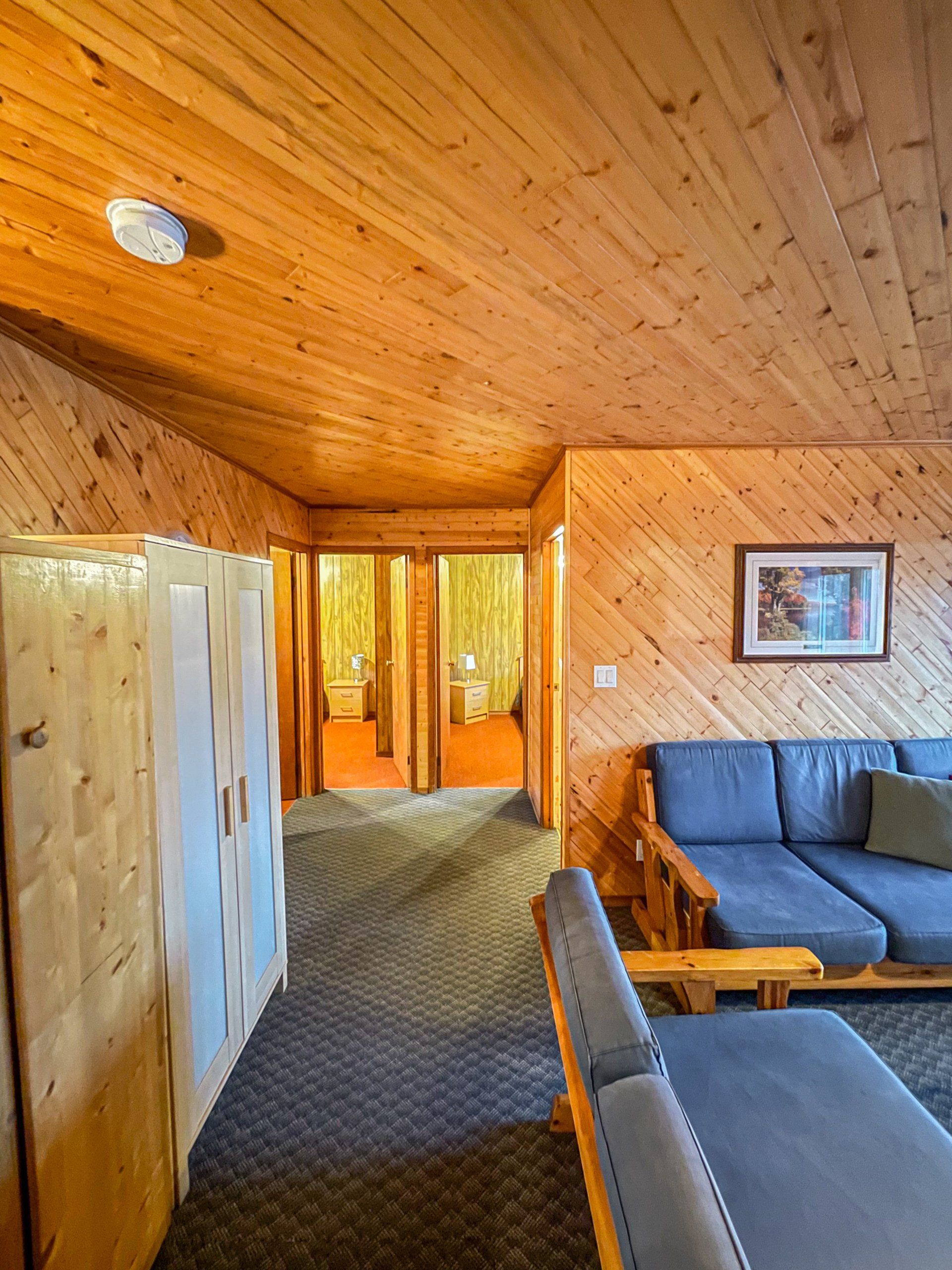 Wood-paneled cabin hallway with a sofa, wardrobe, and doorway leading to a bright room.