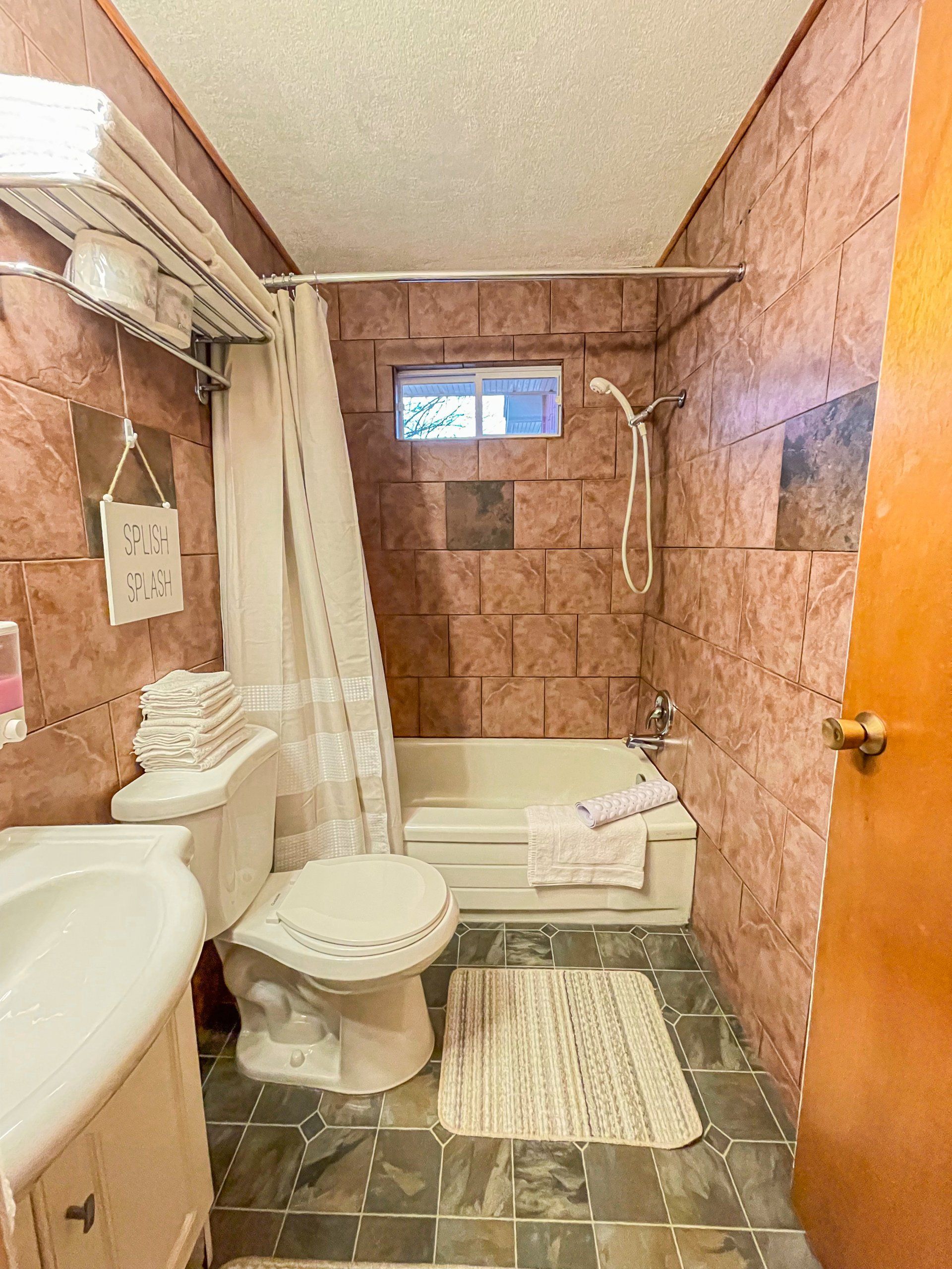 Small pink-tiled bathroom with a toilet, shower curtain, bathtub, sink, and wall-mounted TV.