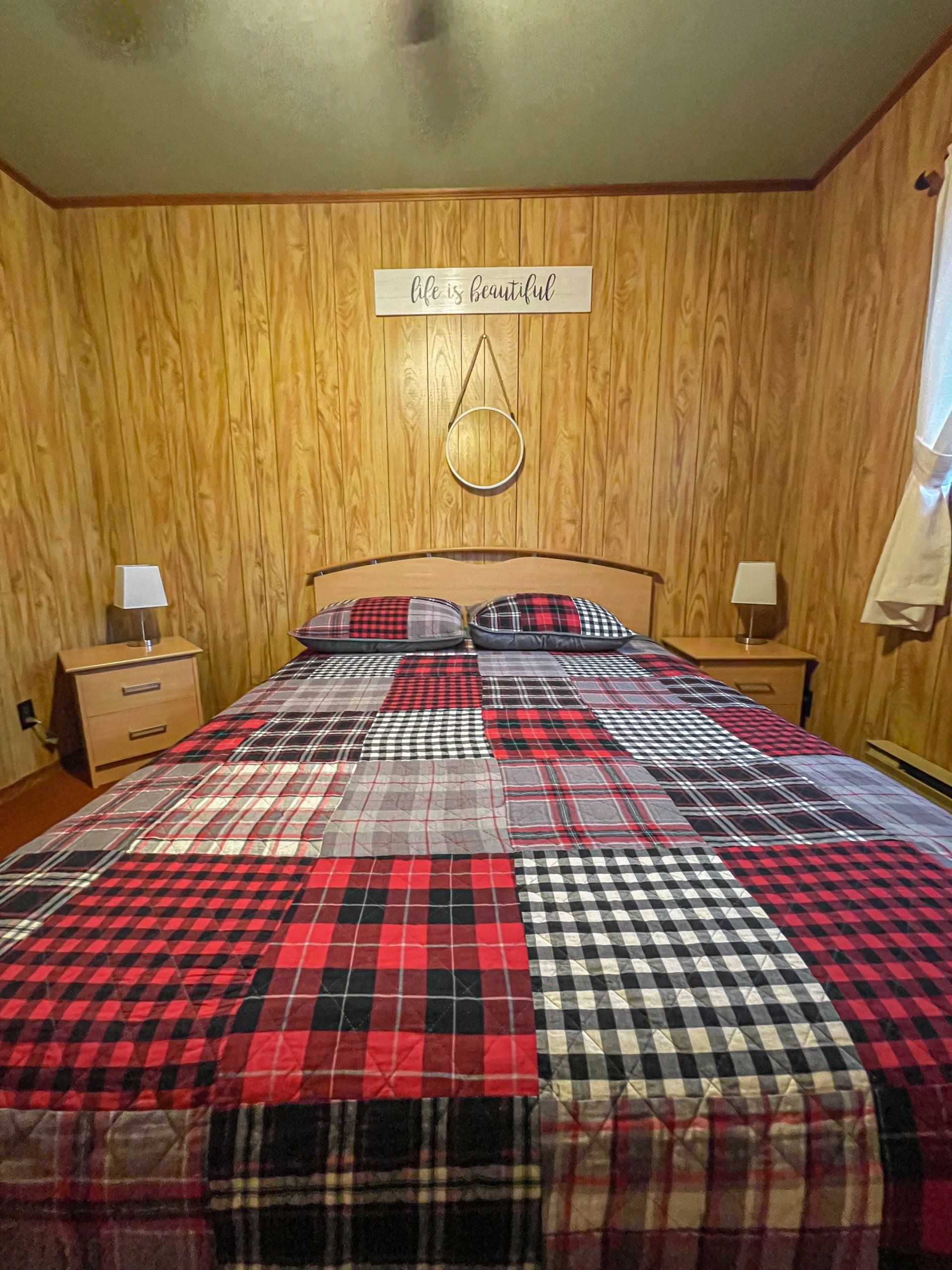Cozy bedroom with a plaid bedspread, wood-paneled walls, and matching bedside tables and lamps.