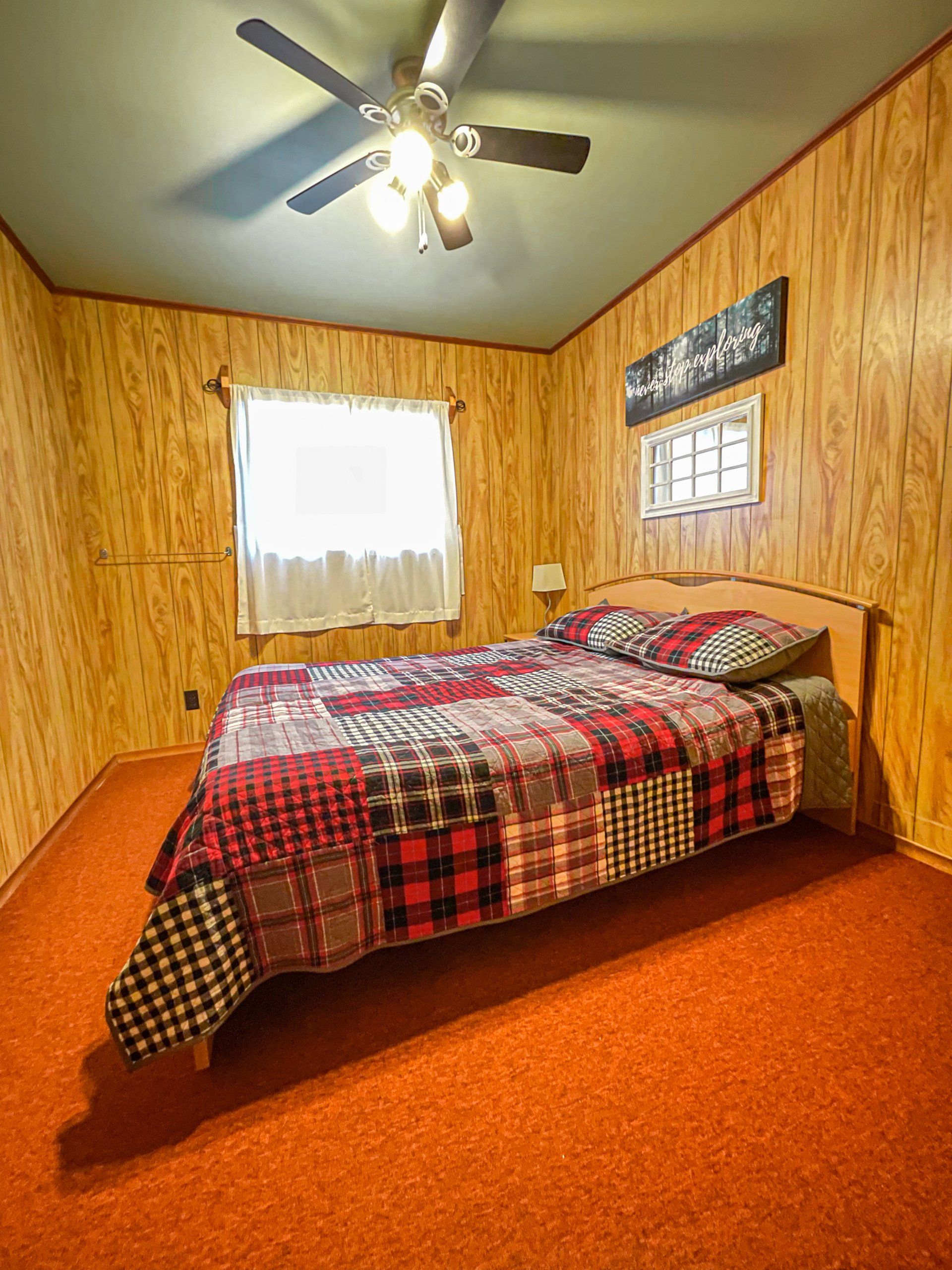 Small bedroom with a red plaid bedspread, wood-paneled walls, and a ceiling fan.