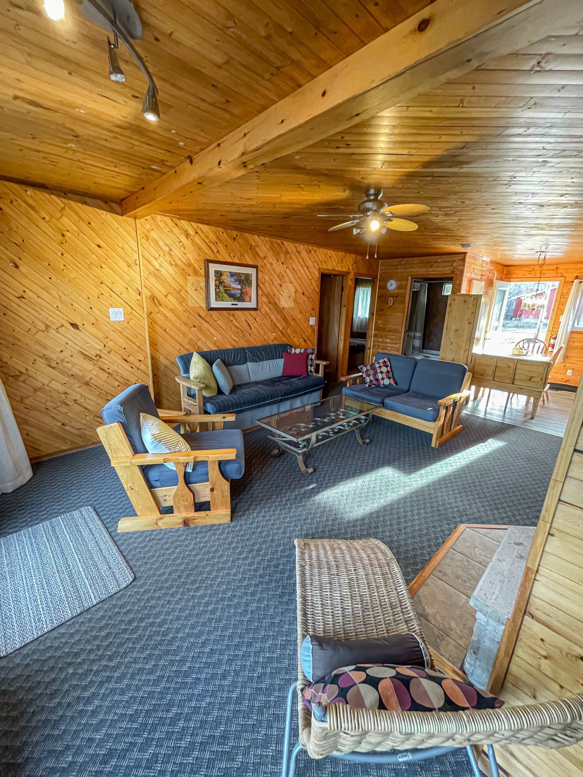 Cozy wood-paneled living room with sofa, armchairs, ceiling fan, rug, and window light